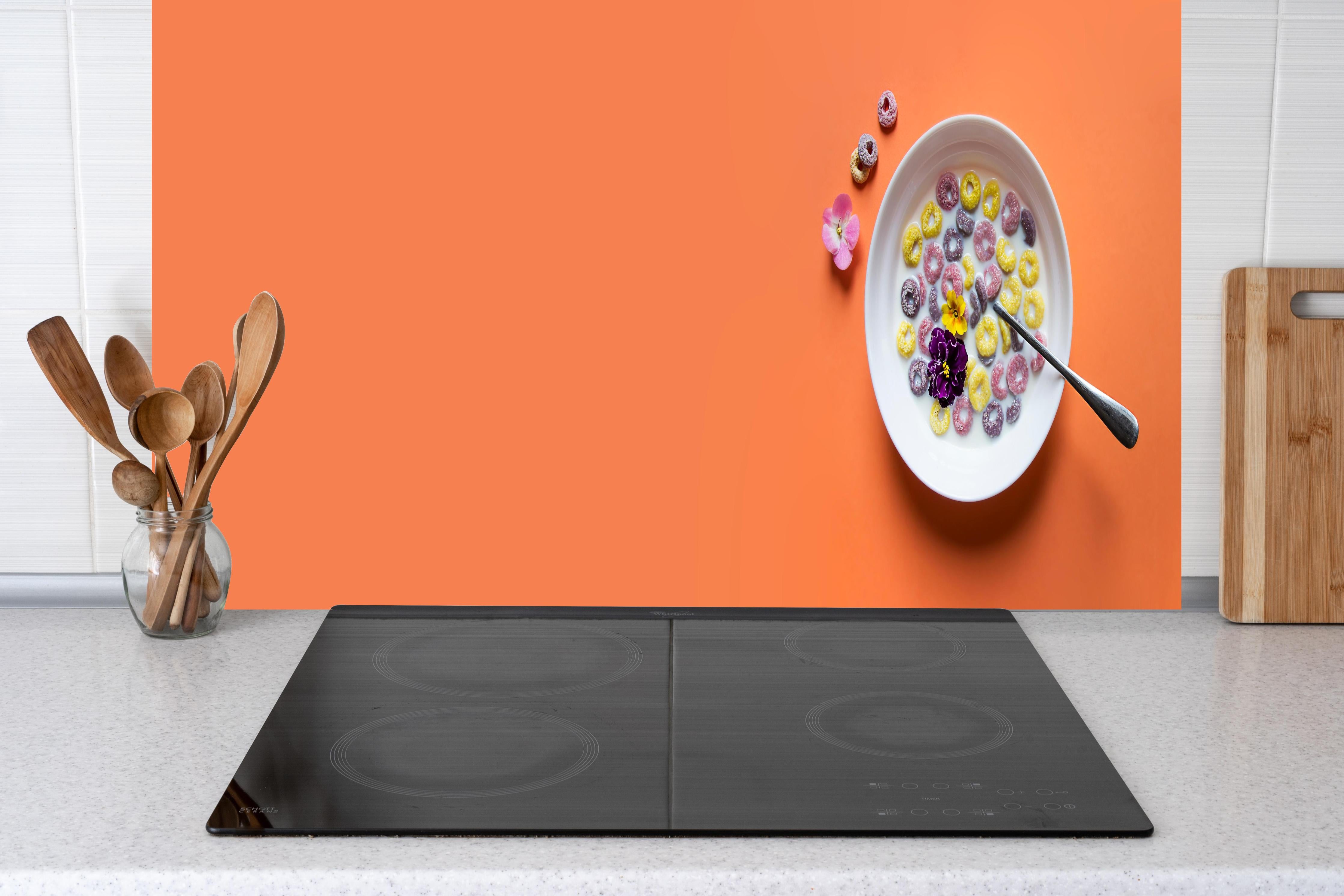 Küche - Orange Frühstücks-Bowl hinter Cerankochfeld und Holz-Kochutensilien