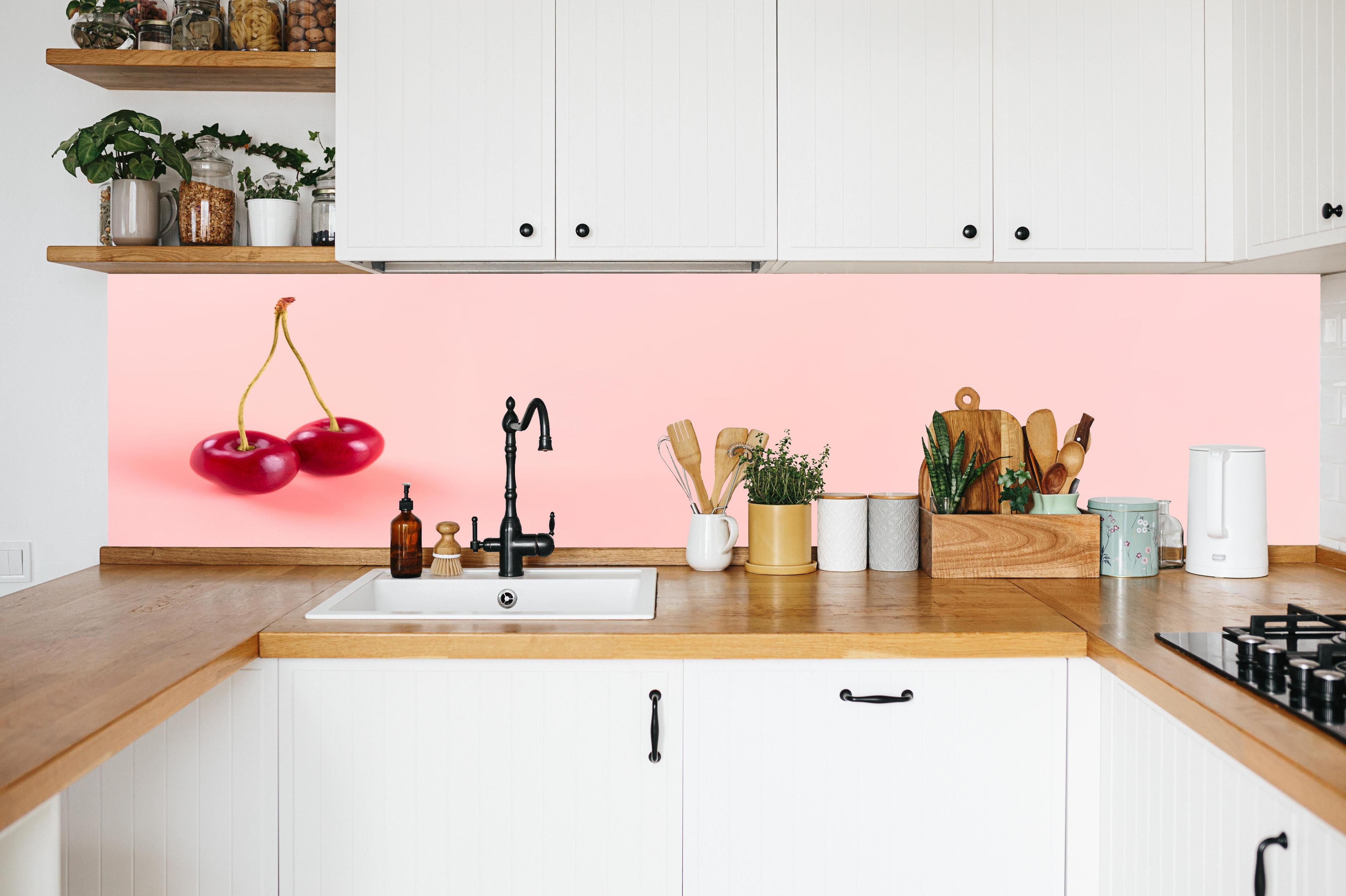 Küche - Rote Kirschen auf Rosa Hintergrund in weißer Küche hinter Gewürzen und Kochlöffeln aus Holz