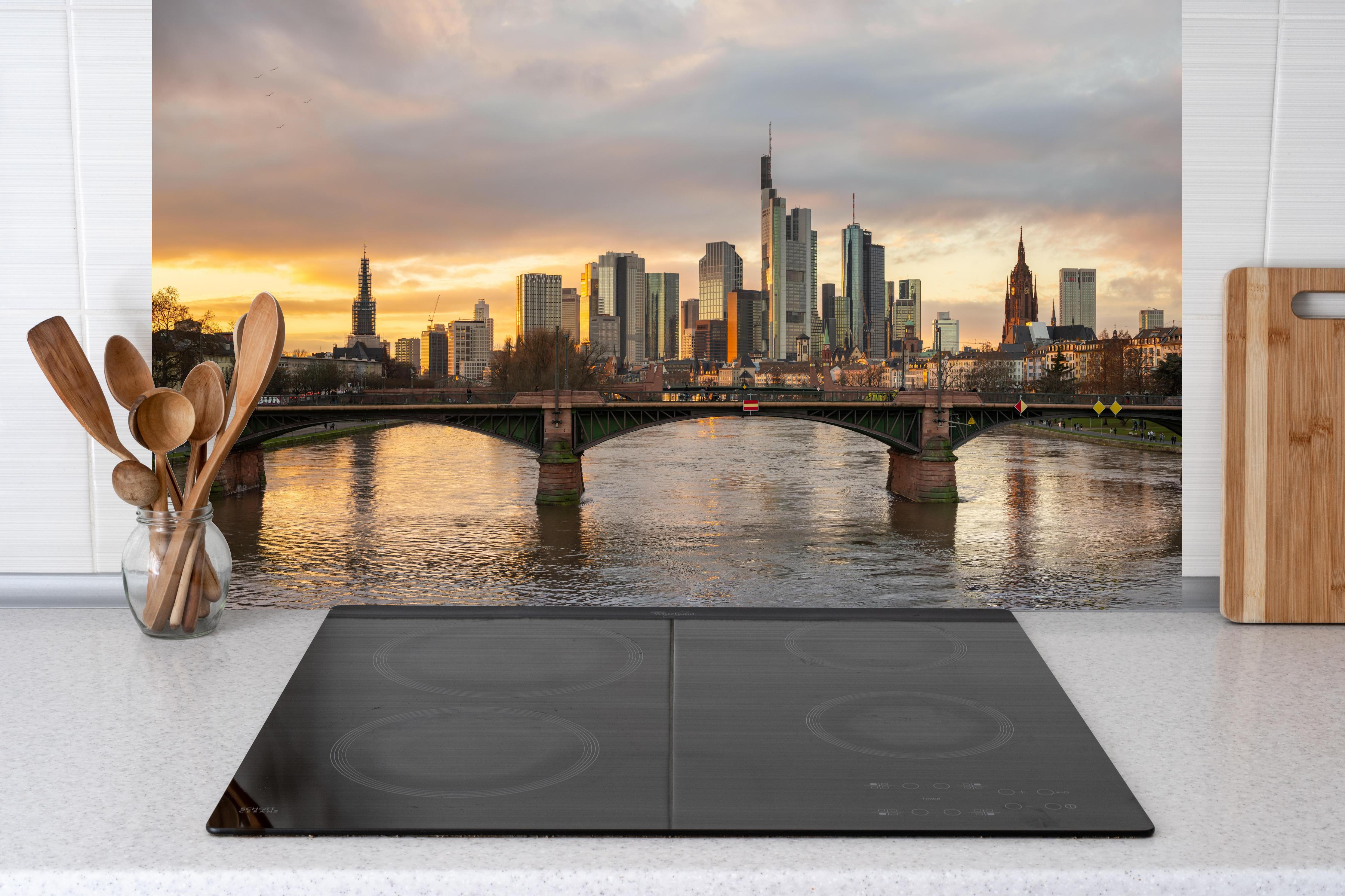 Küche - Stadt-Skyline im Abendlicht hinter Cerankochfeld und Holz-Kochutensilien