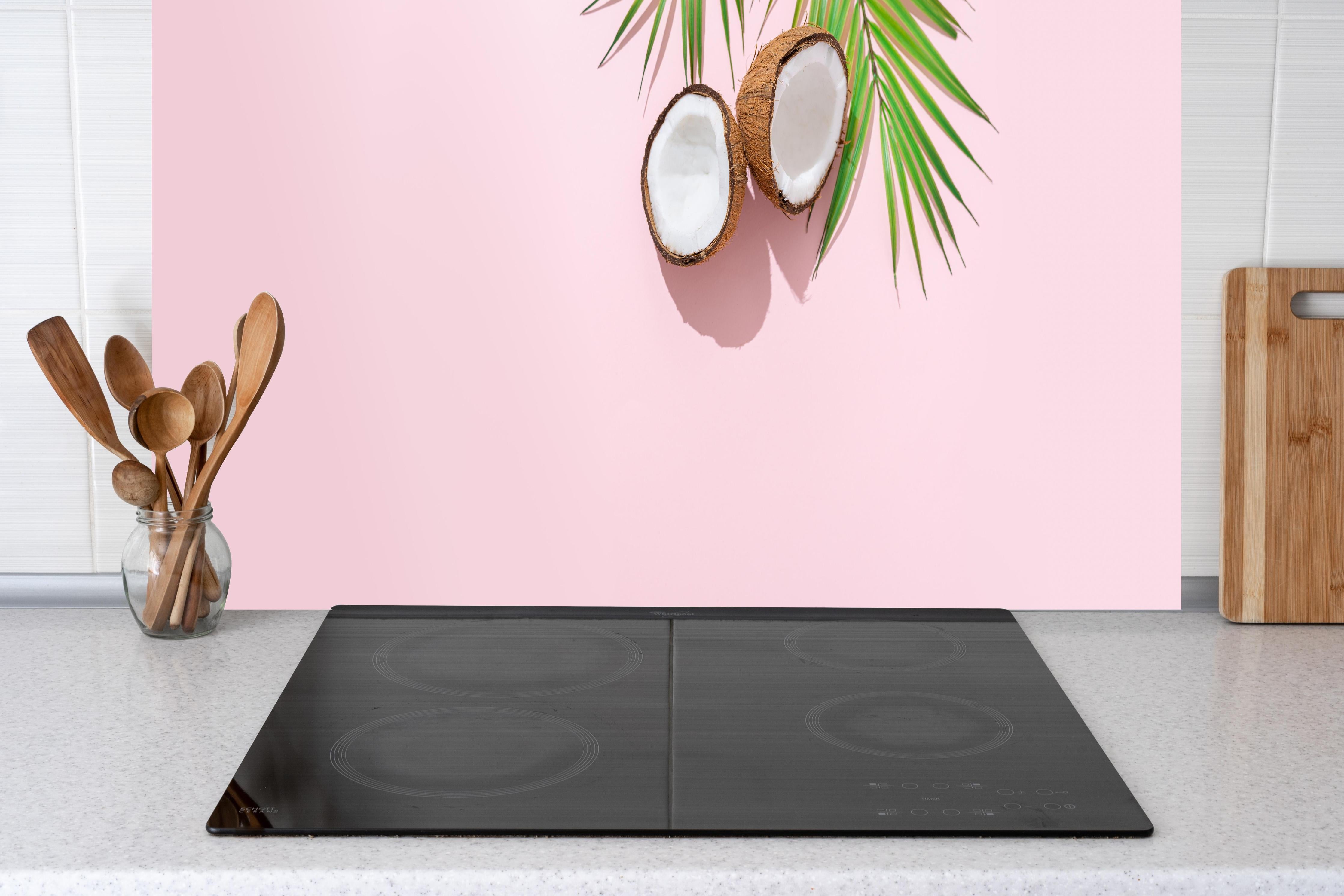 Küche - Tropische Kokosnuss auf Rosa hinter Cerankochfeld und Holz-Kochutensilien