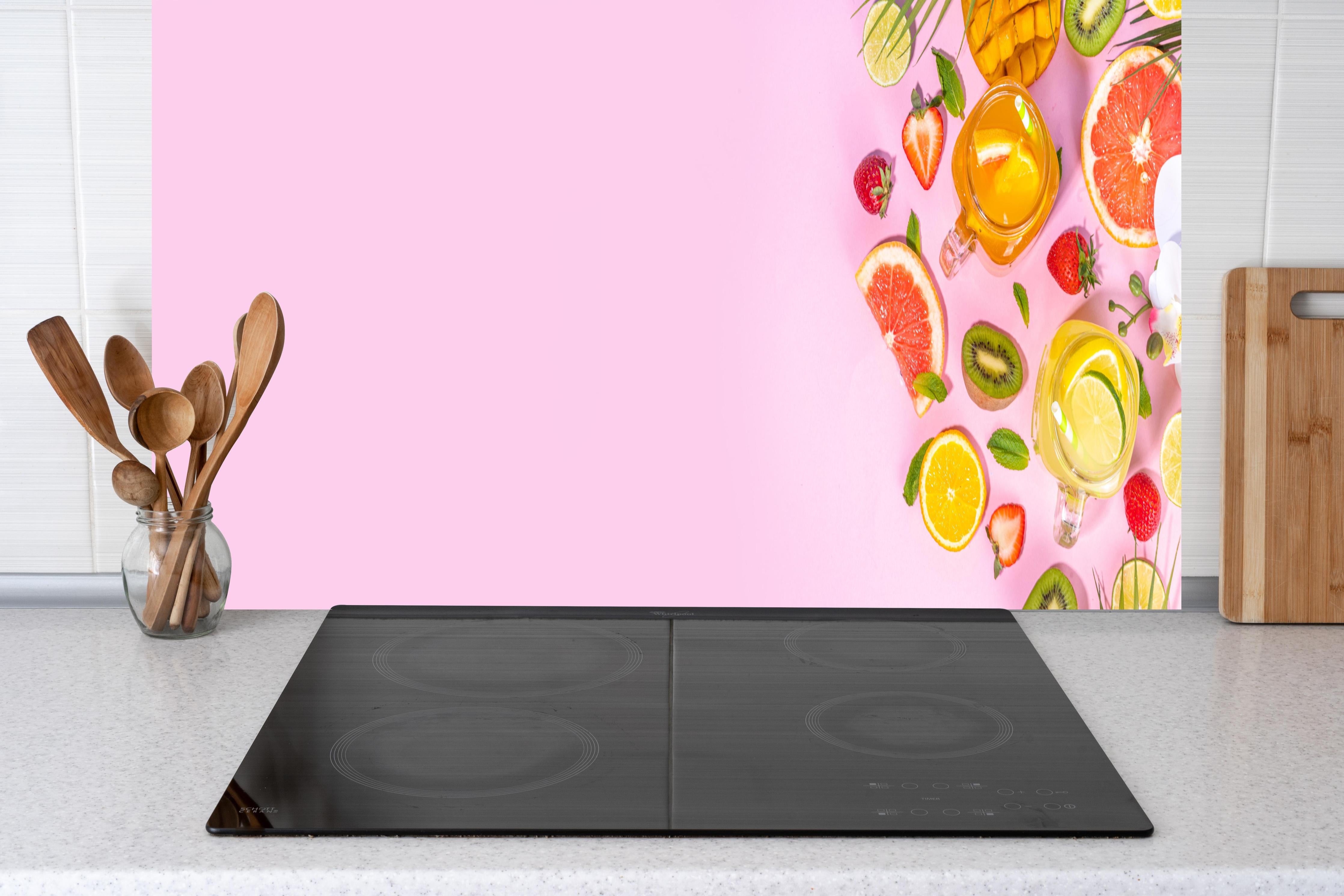 Küche - Zitrusfrüchte auf rosa Hintergrund hinter Cerankochfeld und Holz-Kochutensilien