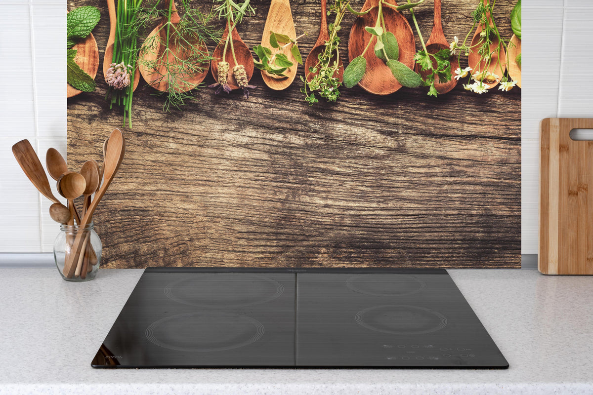 Küche - Frische Kräuter auf Holzplatte hinter Cerankochfeld und Holz-Kochutensilien