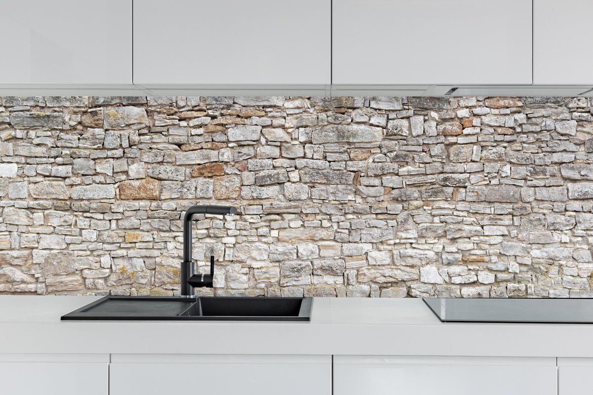Küche - Gräuliche alte Mauer aus groben Steinen hinter weißen Hochglanz-Küchenregalen und schwarzem Wasserhahn