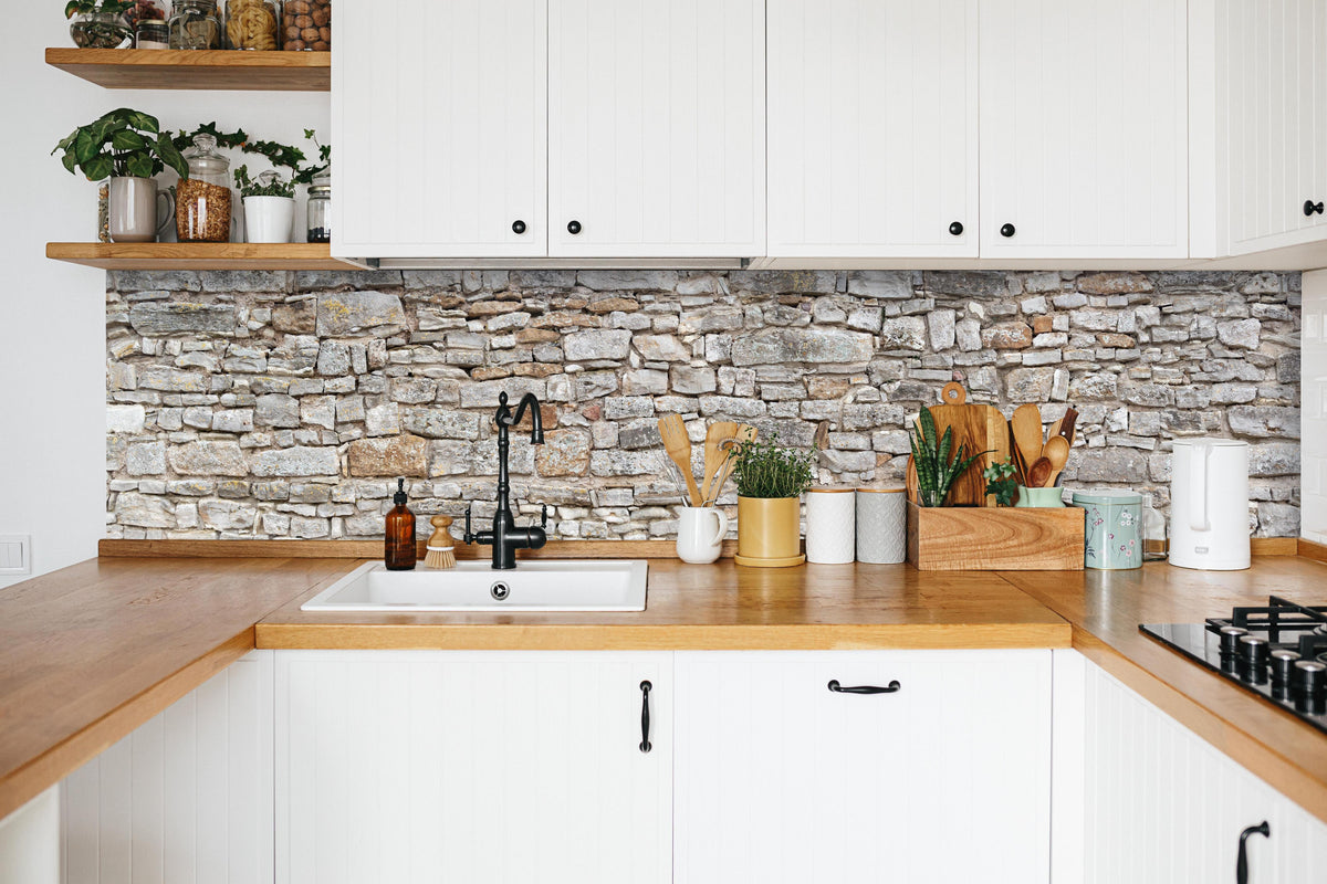 Küche - Gräuliche alte Mauer aus groben Steinen in weißer Küche hinter Gewürzen und Kochlöffeln aus Holz