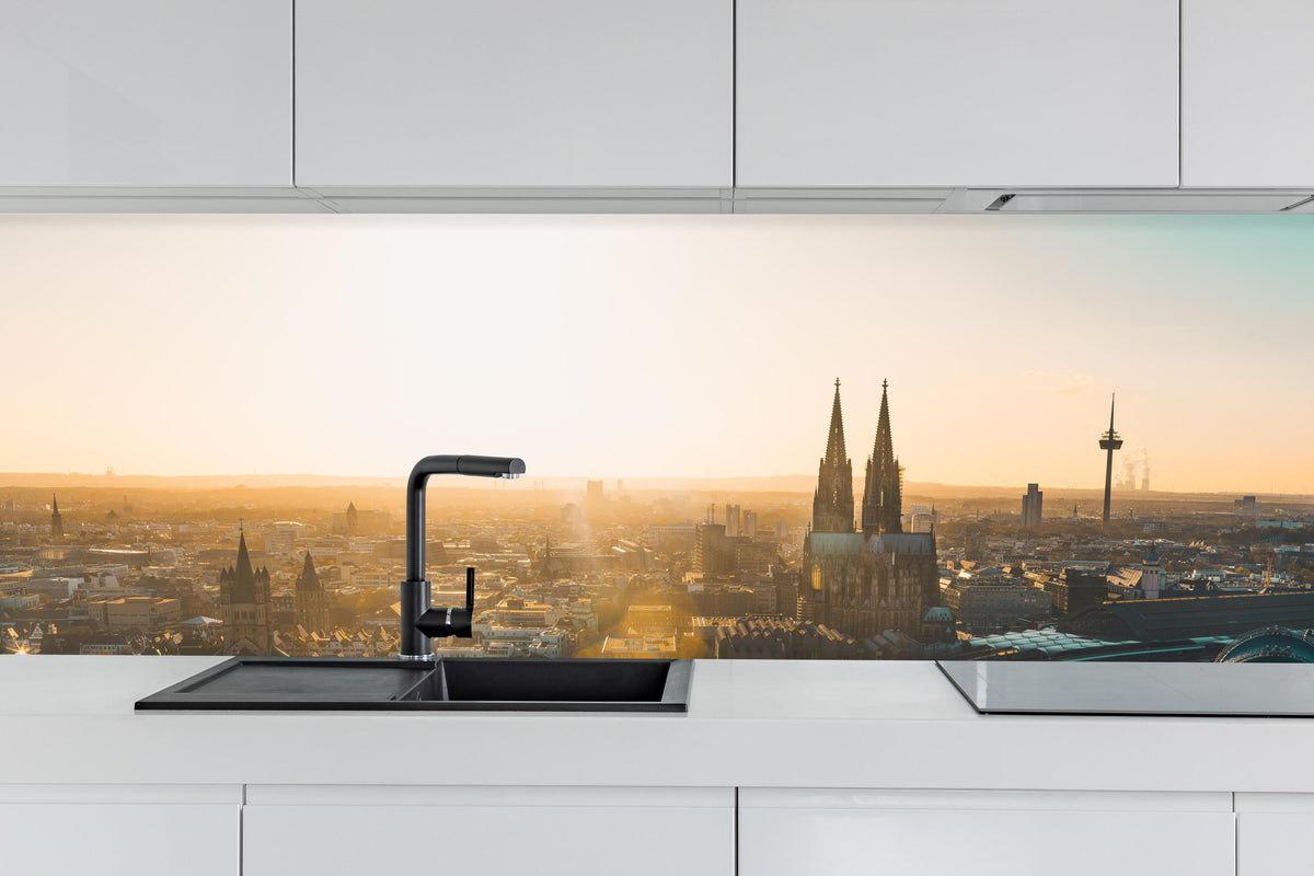 Küche - Panoramablick auf Köln bei Sonnenaufgang hinter weißen Hochglanz-Küchenregalen und schwarzem Wasserhahn