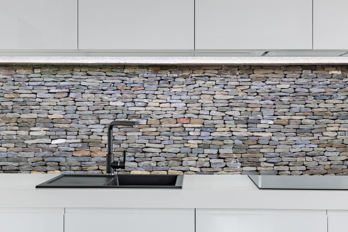 Küche - Pastellfarbene Steinmauer hinter weißen Hochglanz-Küchenregalen und schwarzem Wasserhahn