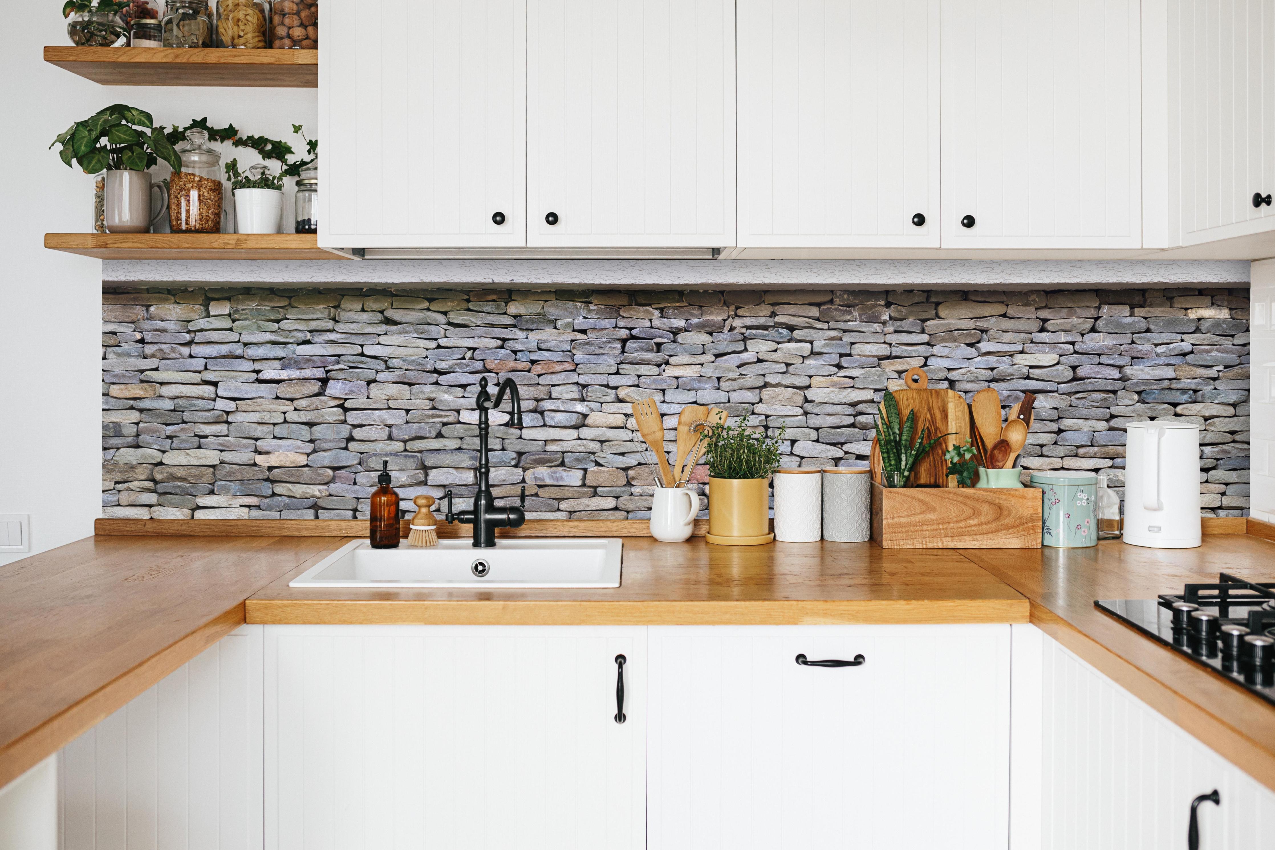 Küche - Pastellfarbene Steinmauer in weißer Küche hinter Gewürzen und Kochlöffeln aus Holz