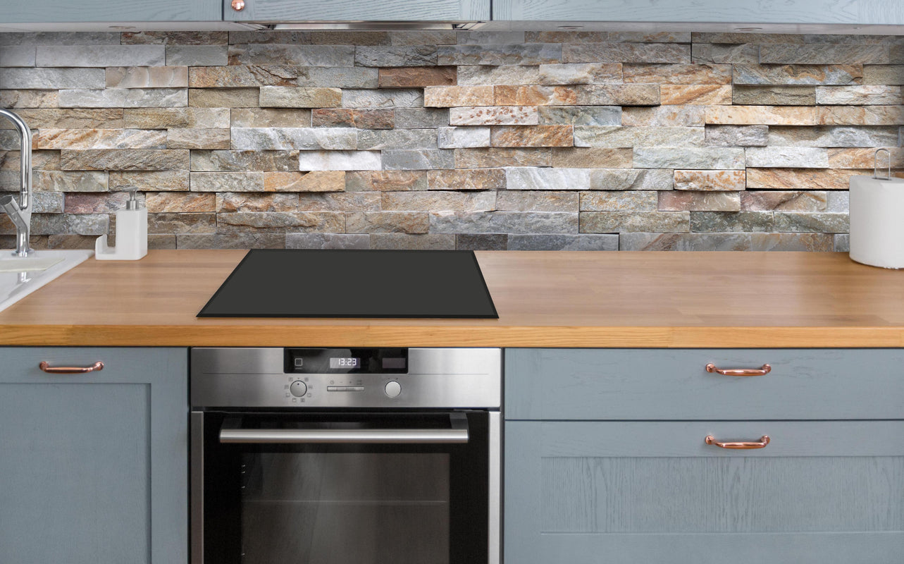 Küche - Pastellfarbige Steinmauer über polierter Holzarbeitsplatte mit Cerankochfeld