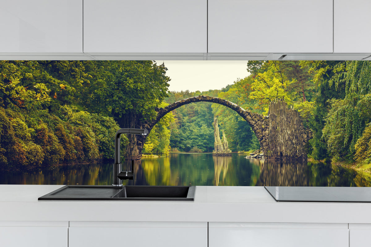 Küche - Rakotz bridge in Kromlau hinter weißen Hochglanz-Küchenregalen und schwarzem Wasserhahn