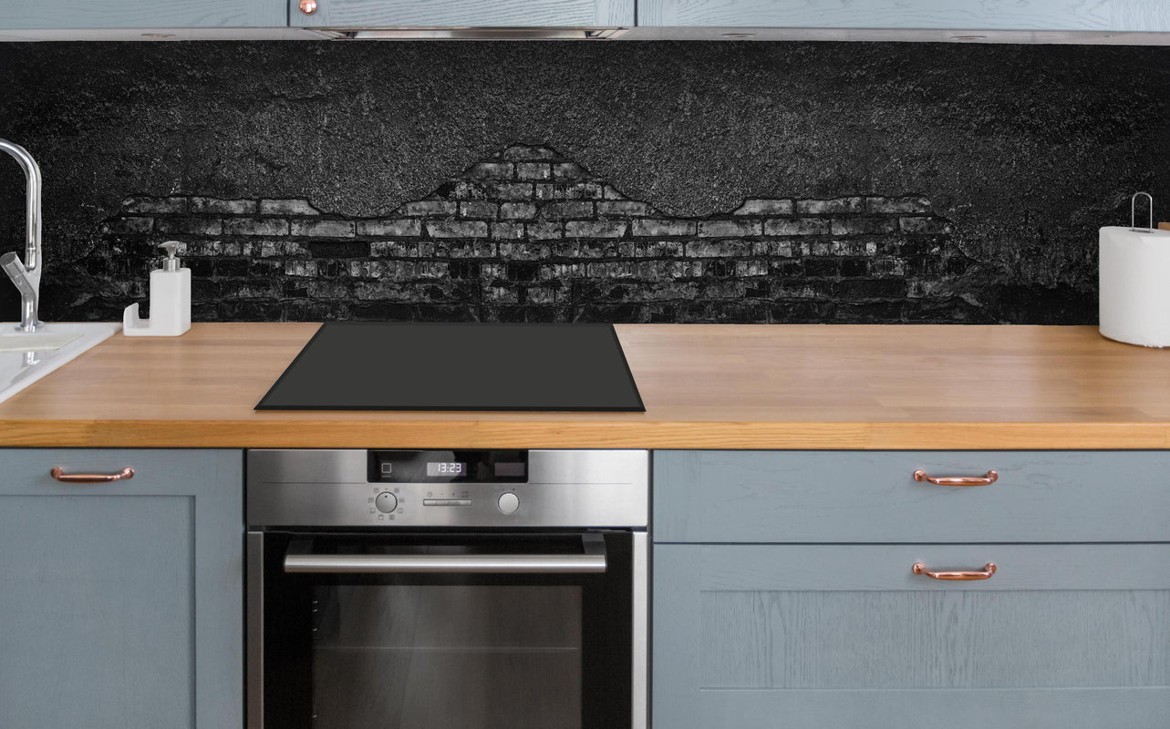 Küche - Schwarz gebrannte Ziegelwand mit abgefallenem Putz über polierter Holzarbeitsplatte mit Cerankochfeld