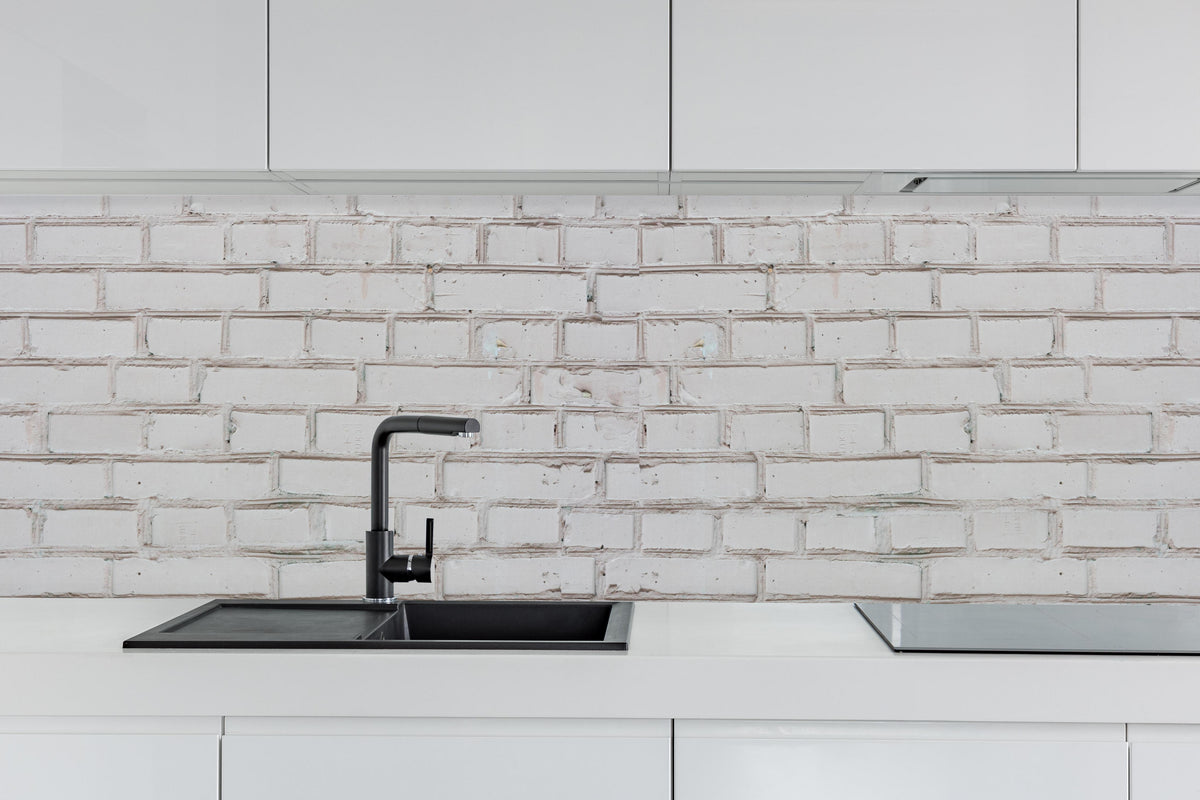Küche - Weiß-Beige Ziegelsteinmauer hinter weißen Hochglanz-Küchenregalen und schwarzem Wasserhahn