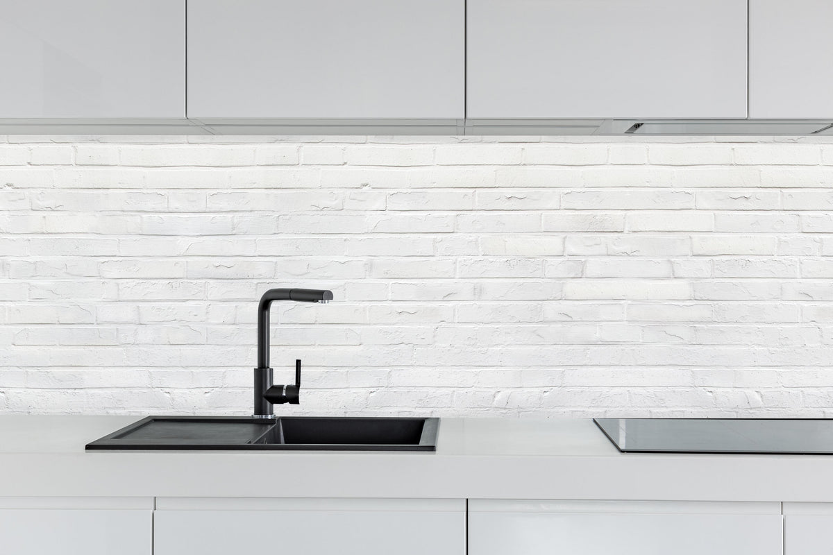 Küche - Weiß bemalte Steinmauer hinter weißen Hochglanz-Küchenregalen und schwarzem Wasserhahn