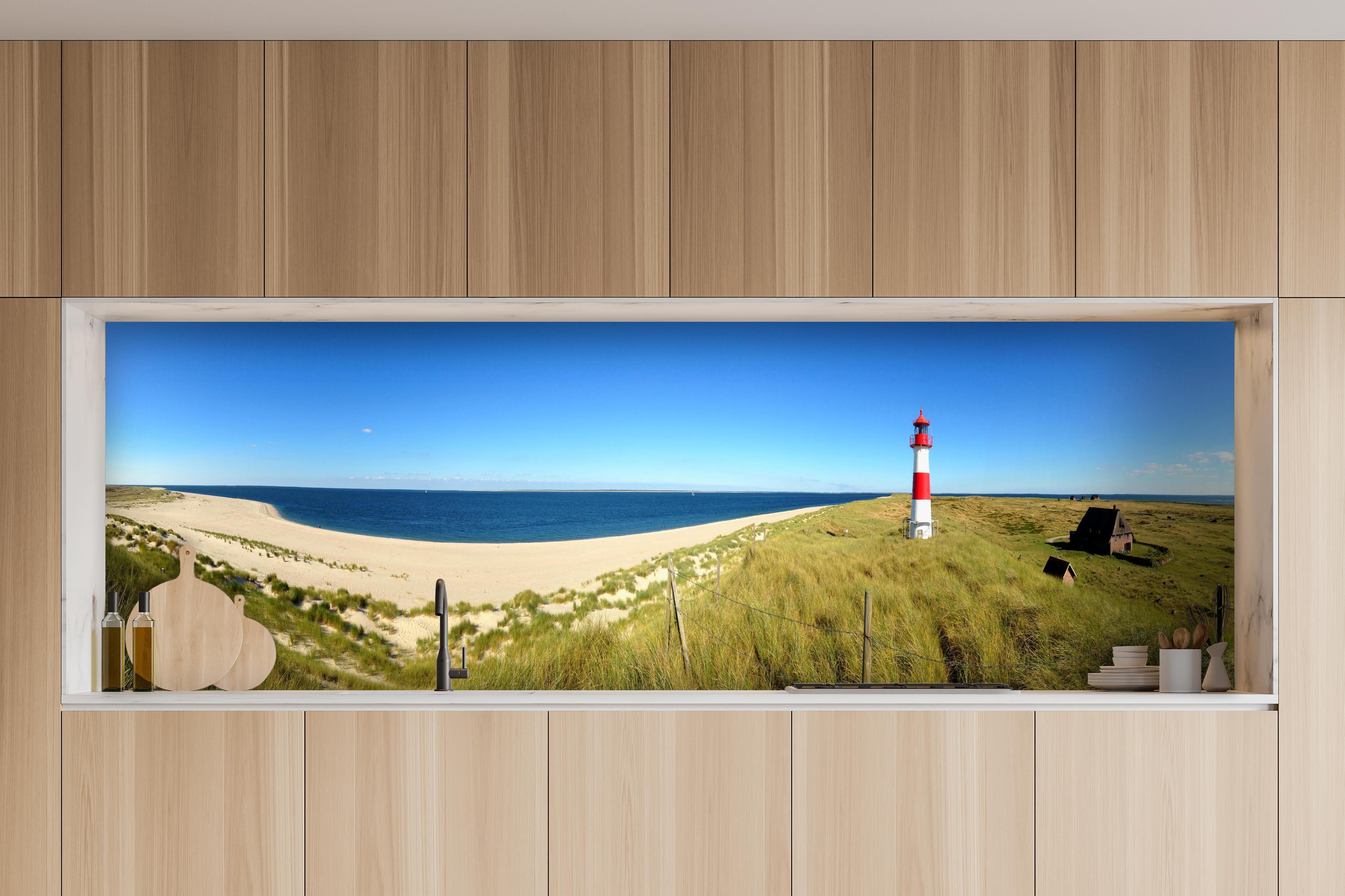 Küche - Leuchtender Leuchtturm an idyllischem Sandstrand hinter weißen Hochglanz-Küchenregalen und schwarzem Wasserhahn