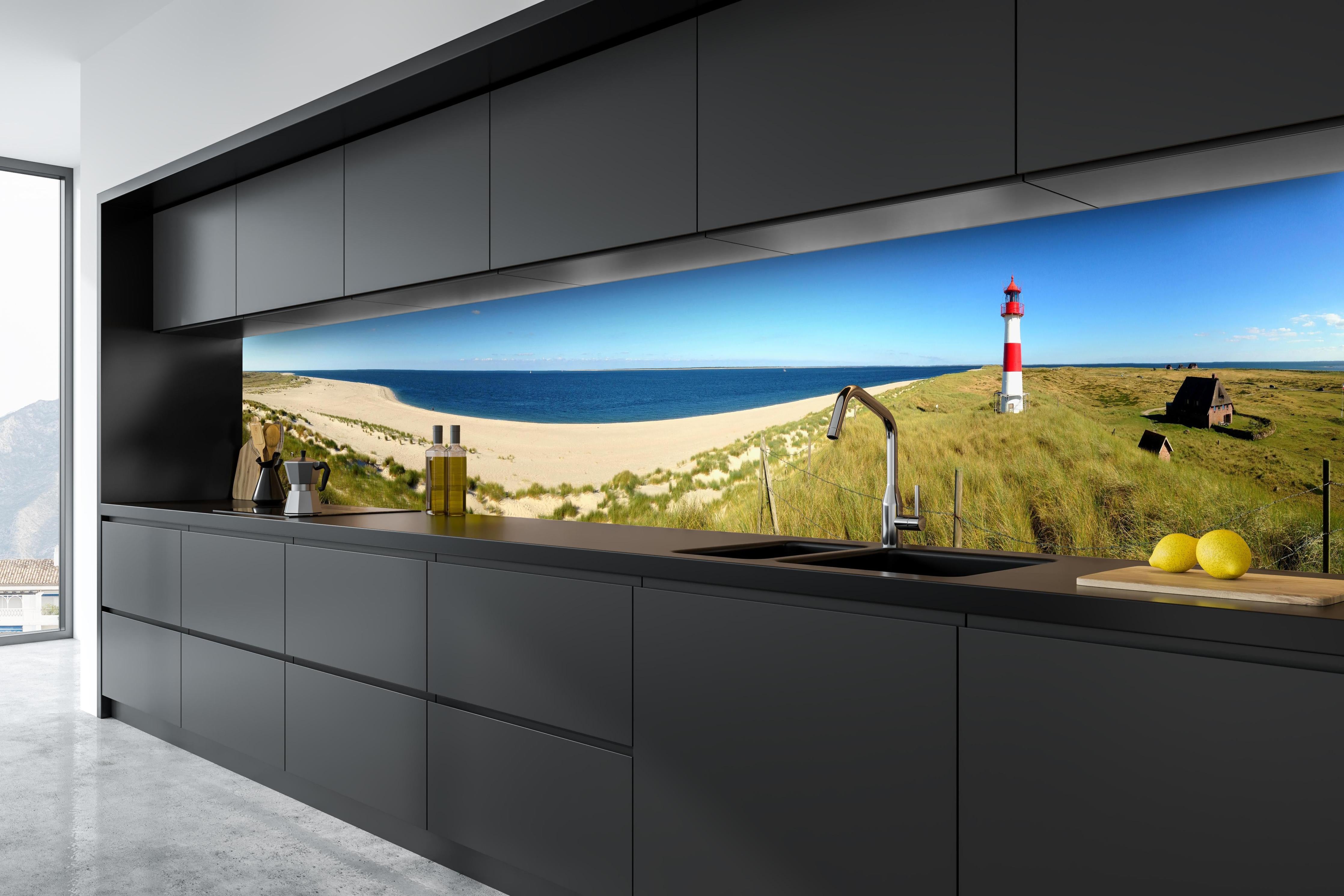 Küche - Leuchtender Leuchtturm an idyllischem Sandstrand hinter weißen Hochglanz-Küchenregalen und schwarzem Wasserhahn