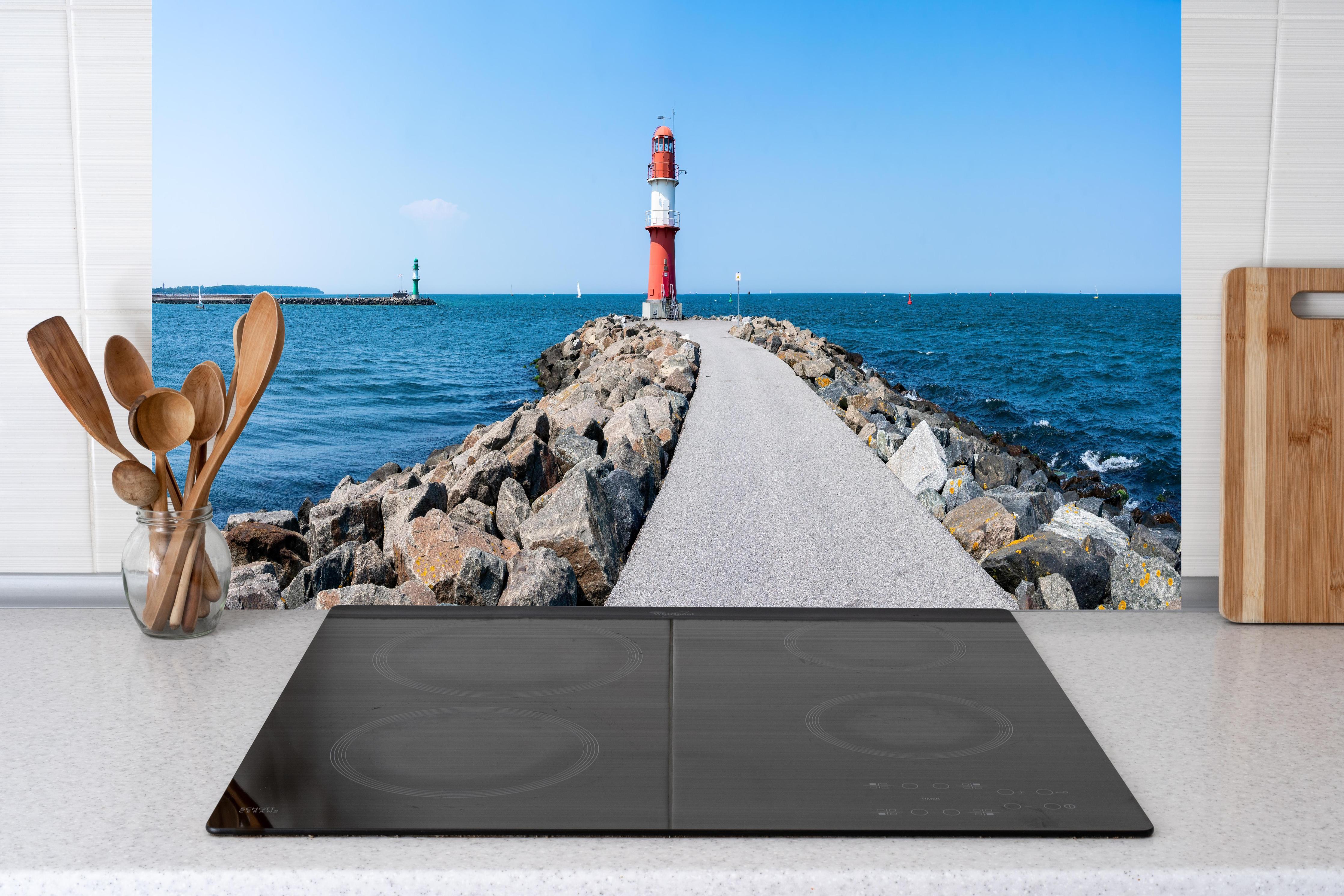 Küche - Leuchtturm an der Küste mit blauer See und klarem Himmel hinter weißen Hochglanz-Küchenregalen und schwarzem Wasserhahn