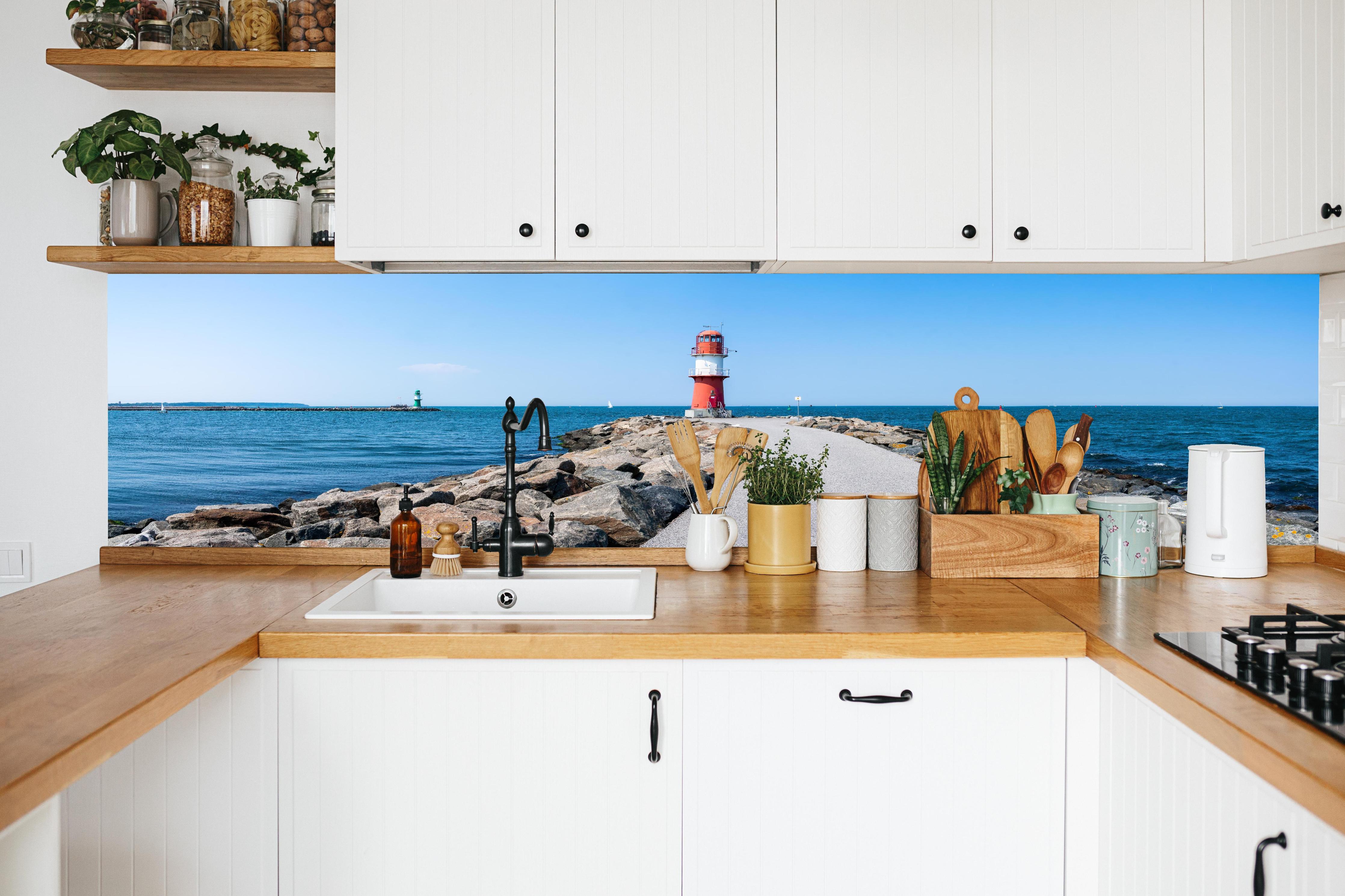 Küche - Leuchtturm an der Küste mit blauer See und klarem Himmel hinter weißen Hochglanz-Küchenregalen und schwarzem Wasserhahn