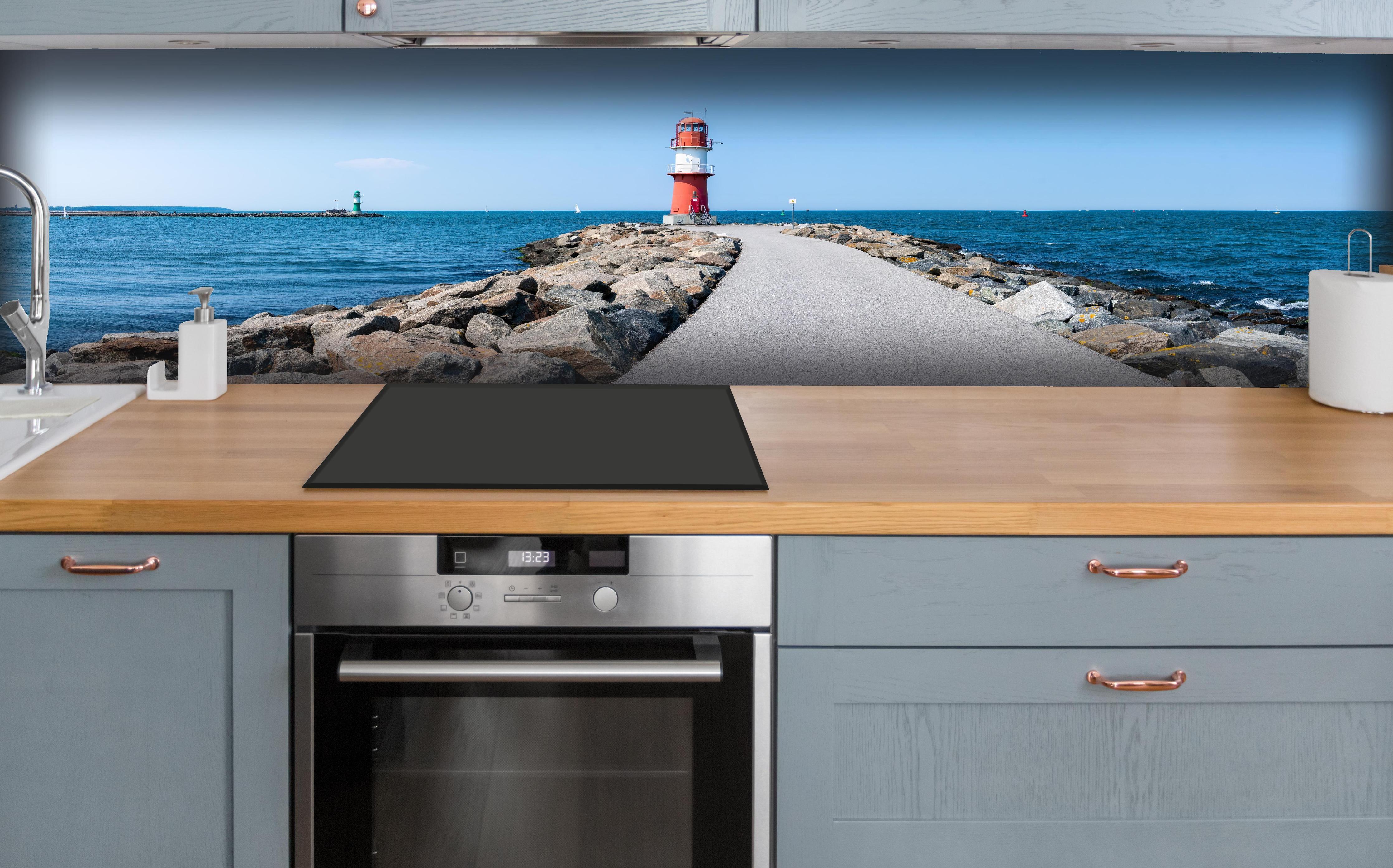 Küche - Leuchtturm an der Küste mit blauer See und klarem Himmel hinter weißen Hochglanz-Küchenregalen und schwarzem Wasserhahn