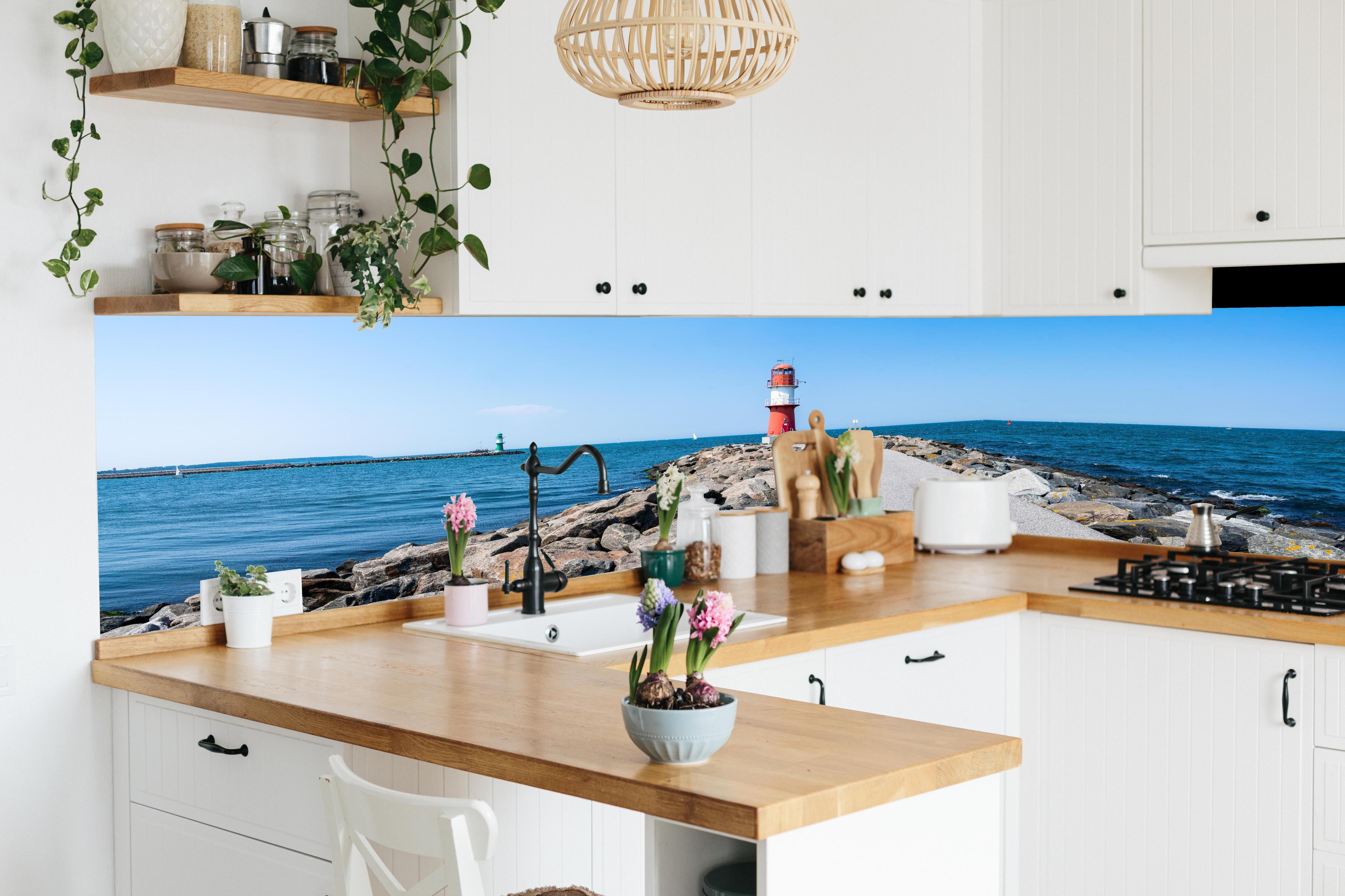 Küche - Leuchtturm an der Küste mit blauer See und klarem Himmel hinter weißen Hochglanz-Küchenregalen und schwarzem Wasserhahn