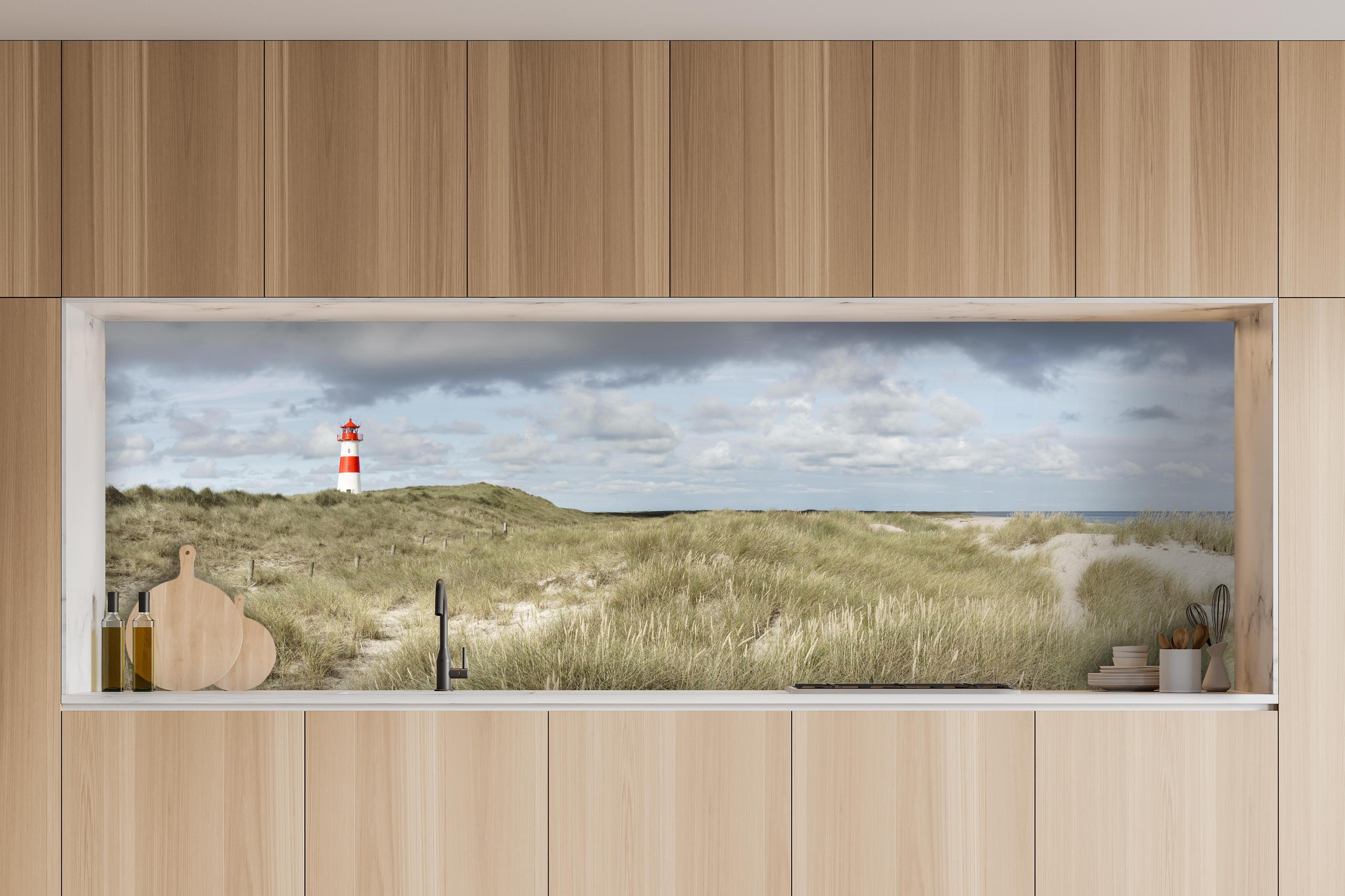Küche - Malerischer Leuchtturm in den Dünen einer Küstenlandschaft hinter weißen Hochglanz-Küchenregalen und schwarzem Wasserhahn