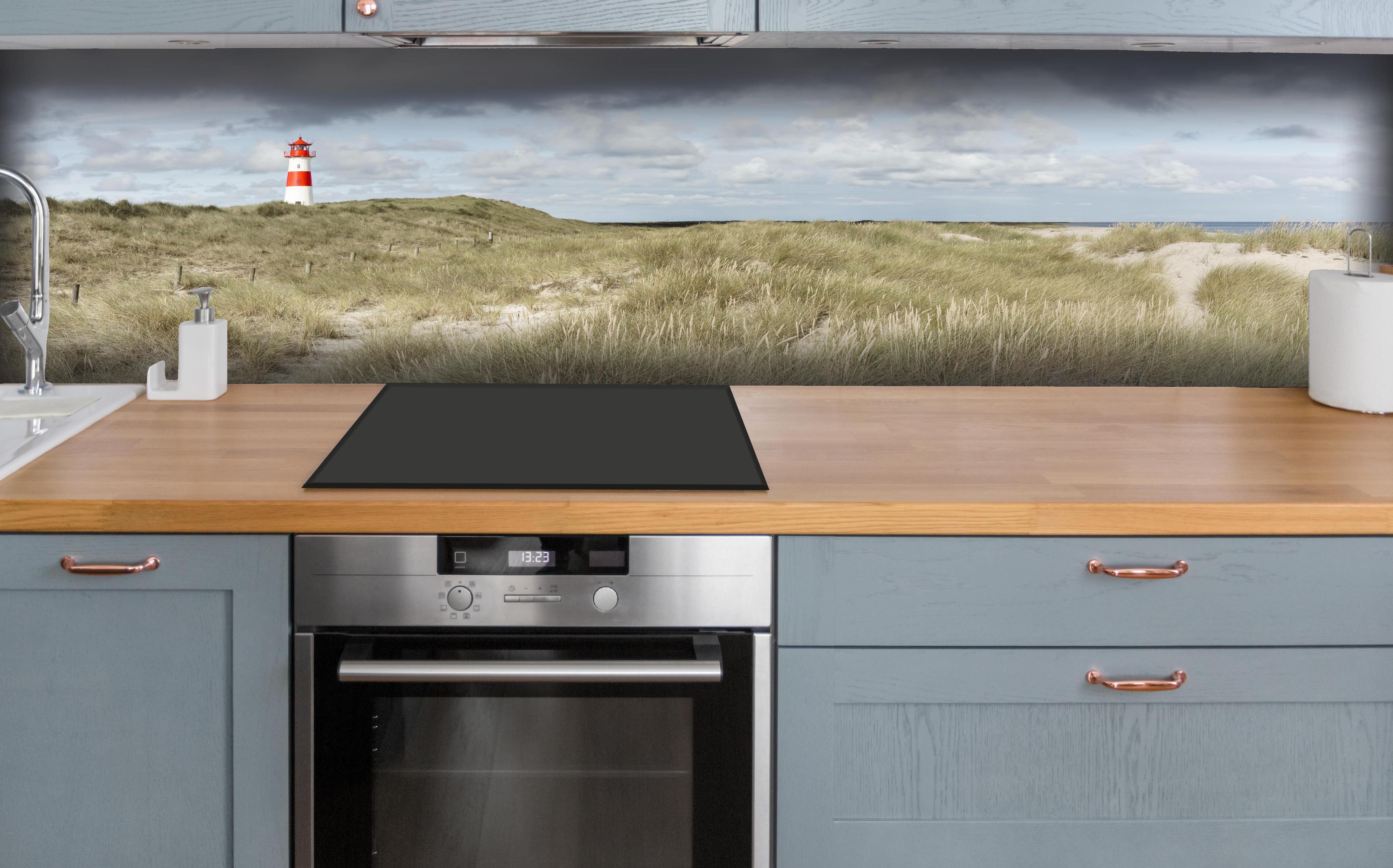 Küche - Malerischer Leuchtturm in den Dünen einer Küstenlandschaft hinter weißen Hochglanz-Küchenregalen und schwarzem Wasserhahn