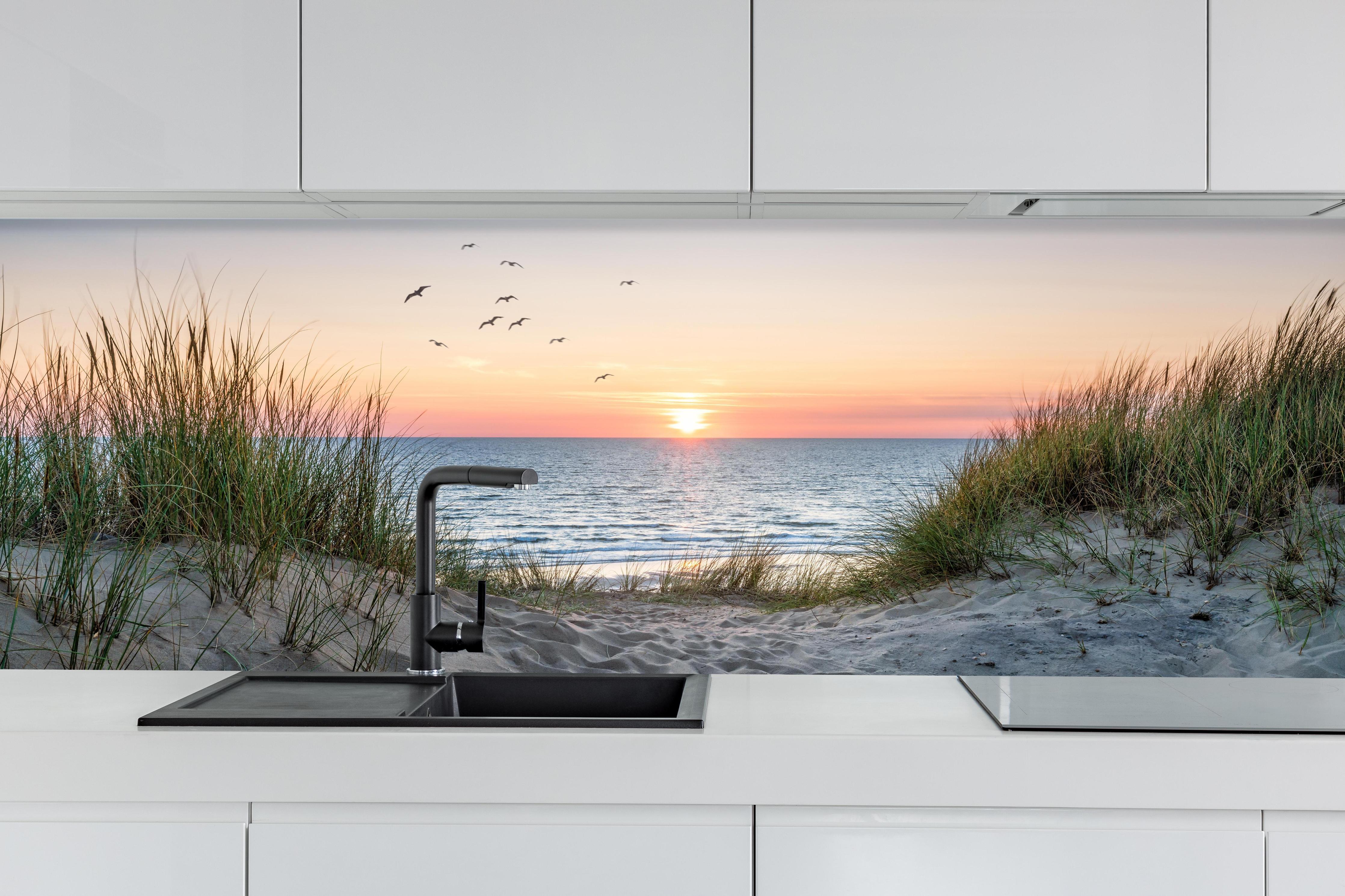 Küche - Malerischer Sonnenuntergang am Dünenstrand hinter weißen Hochglanz-Küchenregalen und schwarzem Wasserhahn