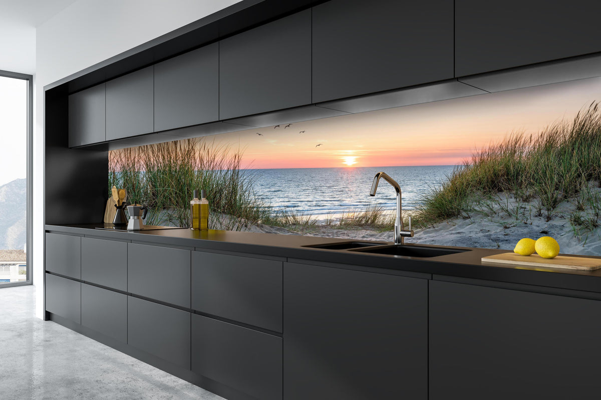 Küche - Malerischer Sonnenuntergang am Dünenstrand hinter weißen Hochglanz-Küchenregalen und schwarzem Wasserhahn