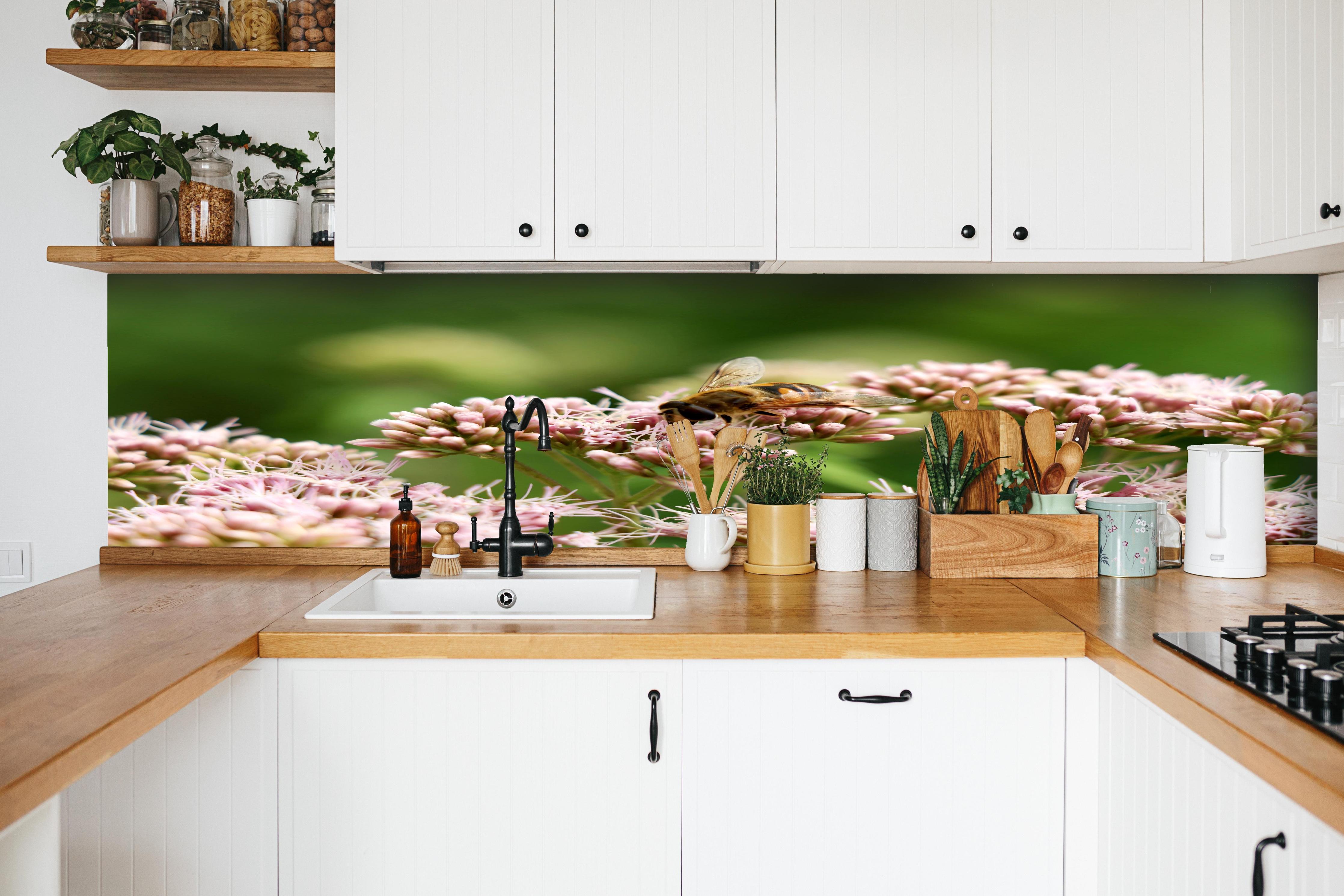 Küche - Nahaufnahme Biene Rosa Blütenpracht hinter weißen Hochglanz-Küchenregalen und schwarzem Wasserhahn