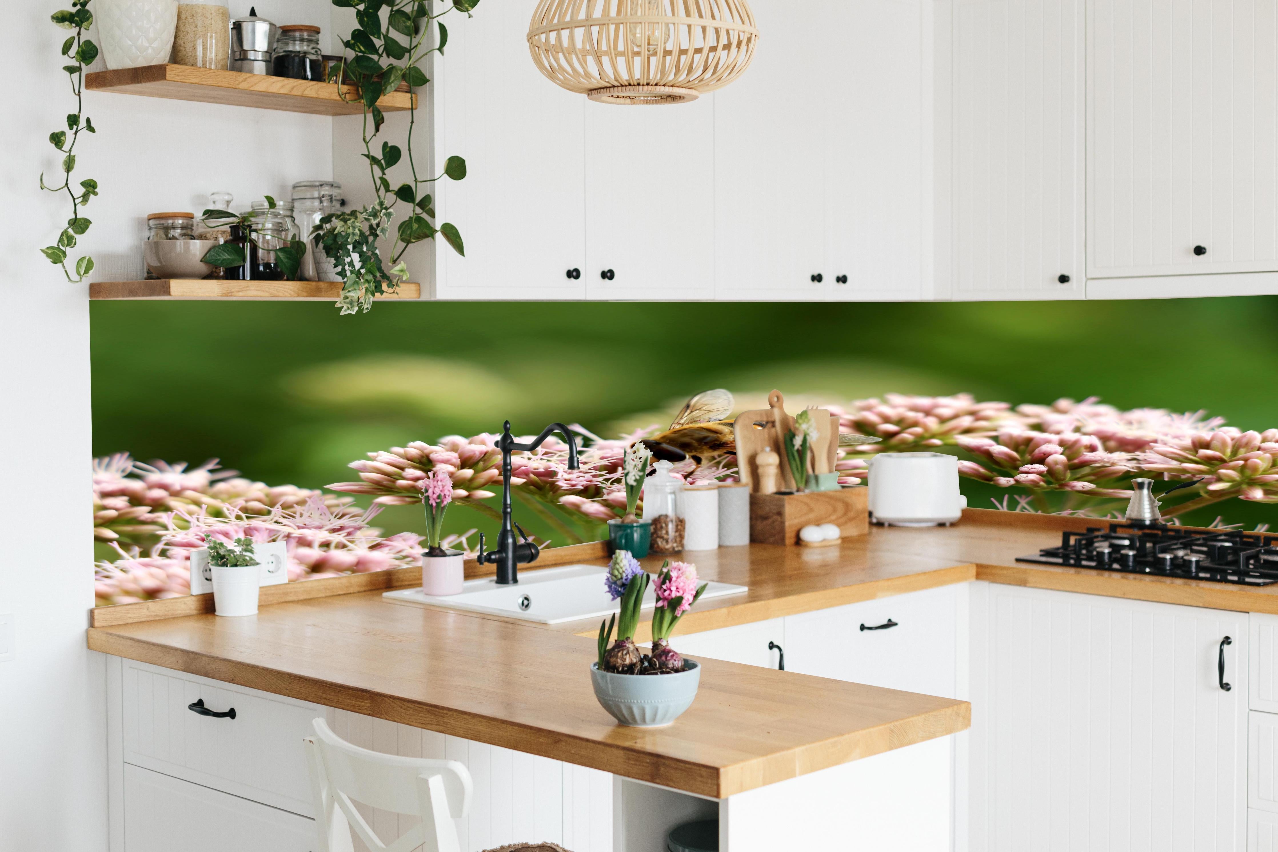 Küche - Nahaufnahme Biene Rosa Blütenpracht hinter weißen Hochglanz-Küchenregalen und schwarzem Wasserhahn