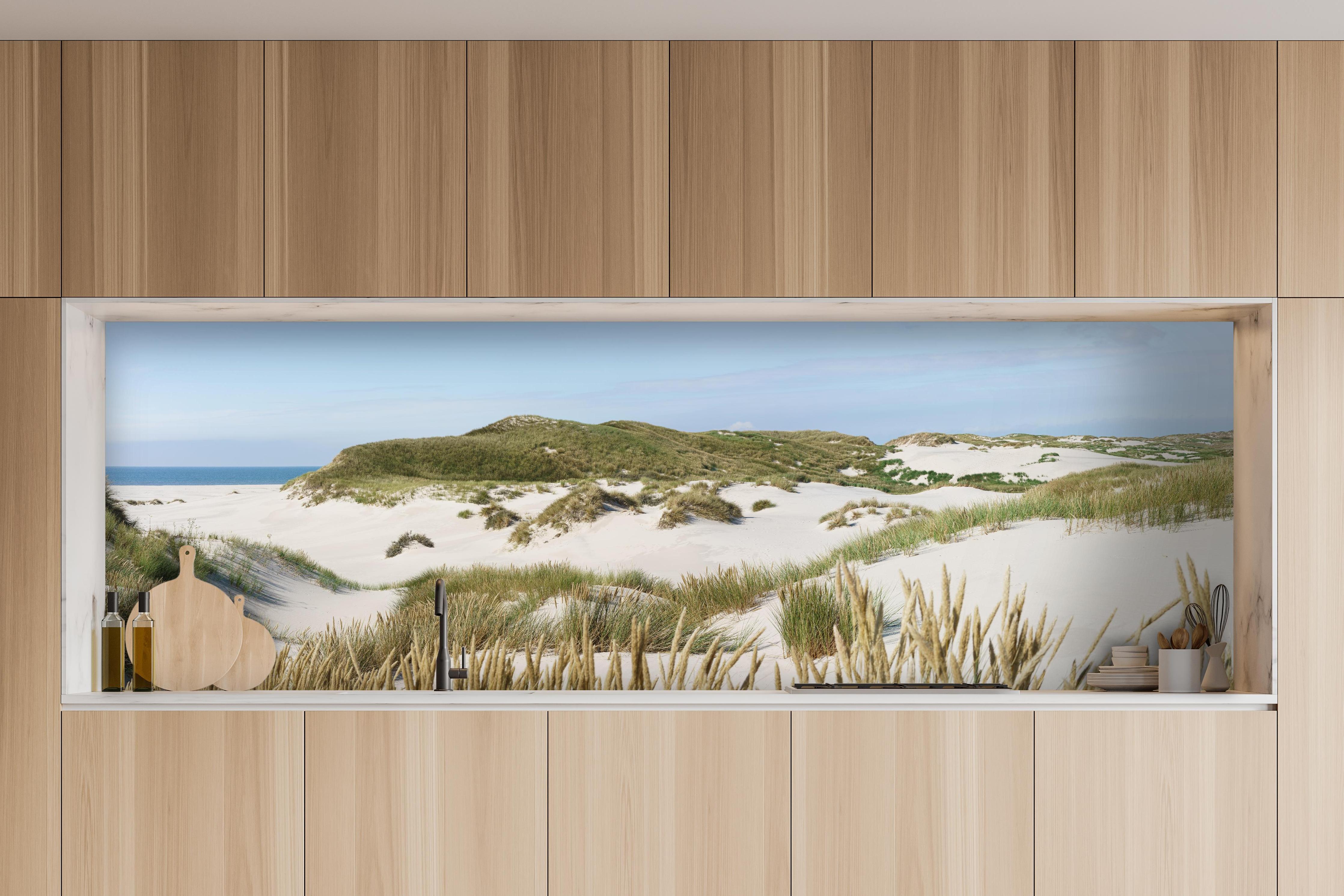 Küche - Naturbelassene Sanddünen mit grasbewachsenen Hügeln und Meerblick hinter weißen Hochglanz-Küchenregalen und schwarzem Wasserhahn
