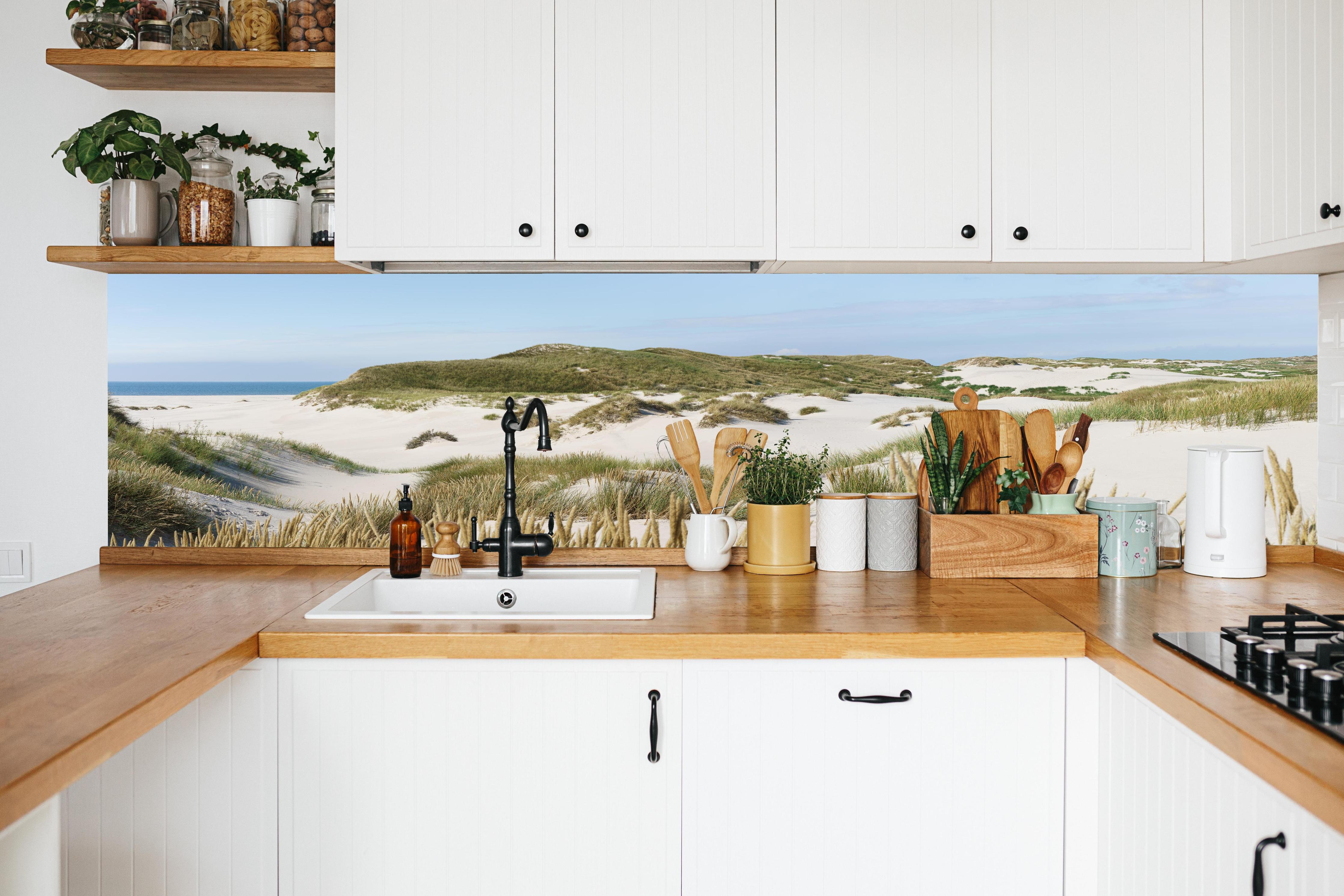 Küche - Naturbelassene Sanddünen mit grasbewachsenen Hügeln und Meerblick hinter weißen Hochglanz-Küchenregalen und schwarzem Wasserhahn