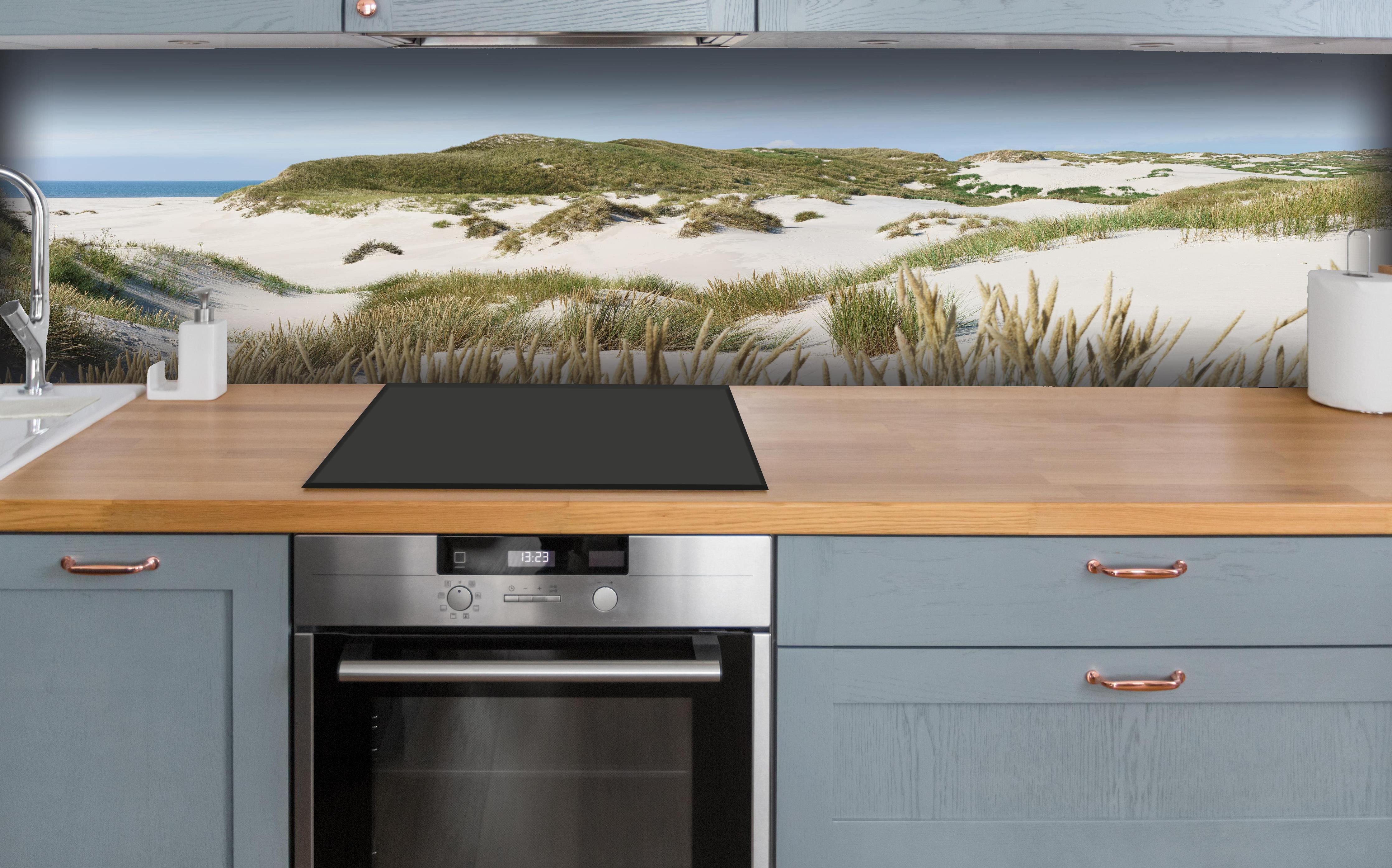 Küche - Naturbelassene Sanddünen mit grasbewachsenen Hügeln und Meerblick hinter weißen Hochglanz-Küchenregalen und schwarzem Wasserhahn