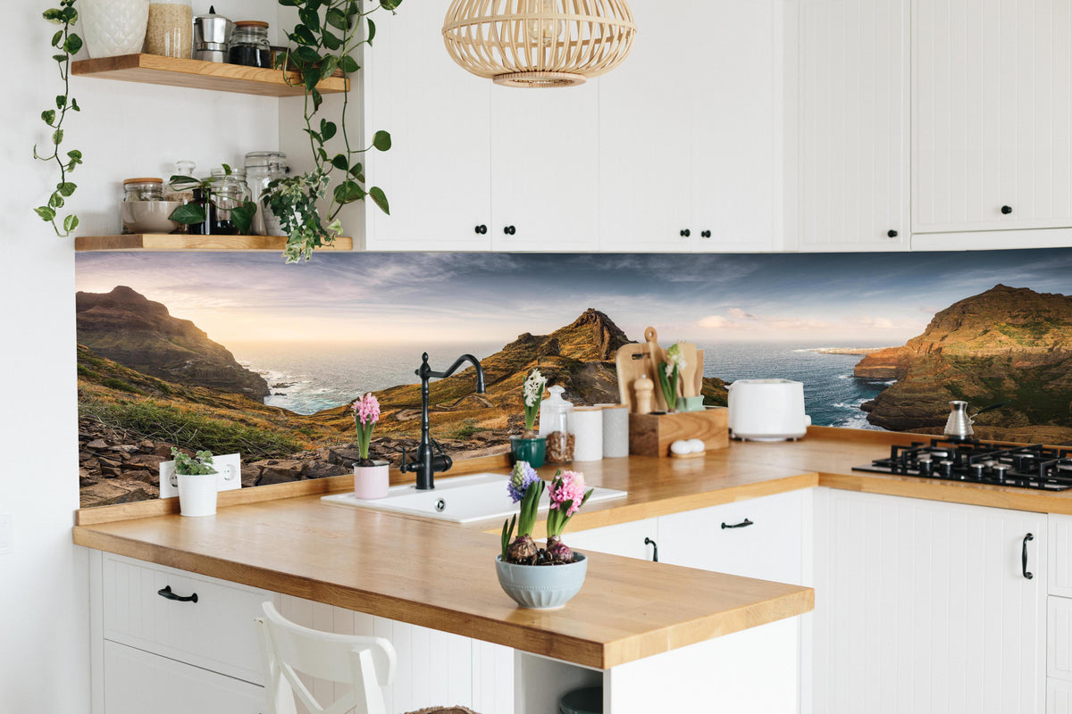 Küche - Panorama des Kap Verde Küstenpfads hinter weißen Hochglanz-Küchenregalen und schwarzem Wasserhahn