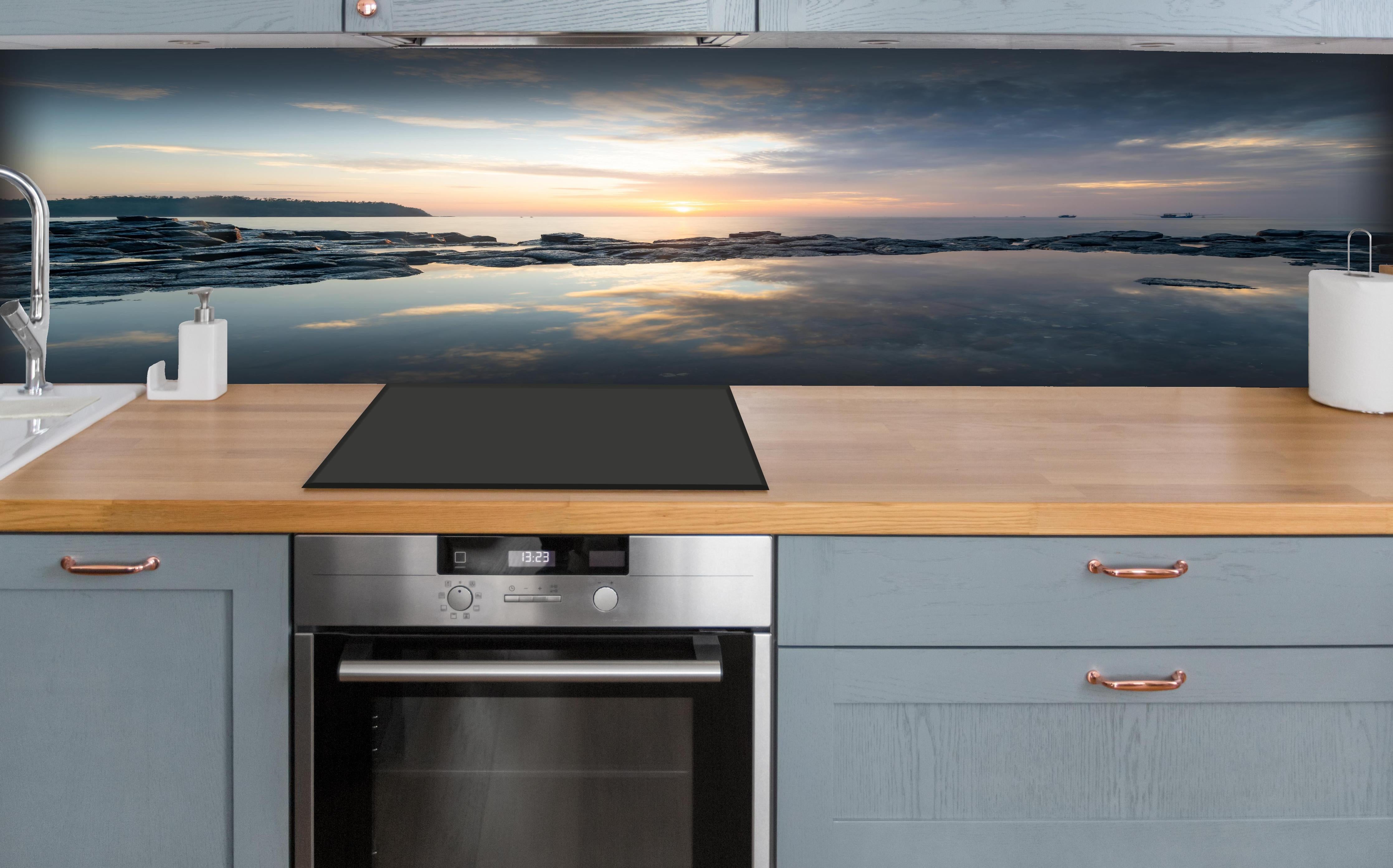 Küche - Pittoresker Sonnenuntergang über dem ruhigen Meer mit reflektierendem Wasser hinter weißen Hochglanz-Küchenregalen und schwarzem Wasserhahn