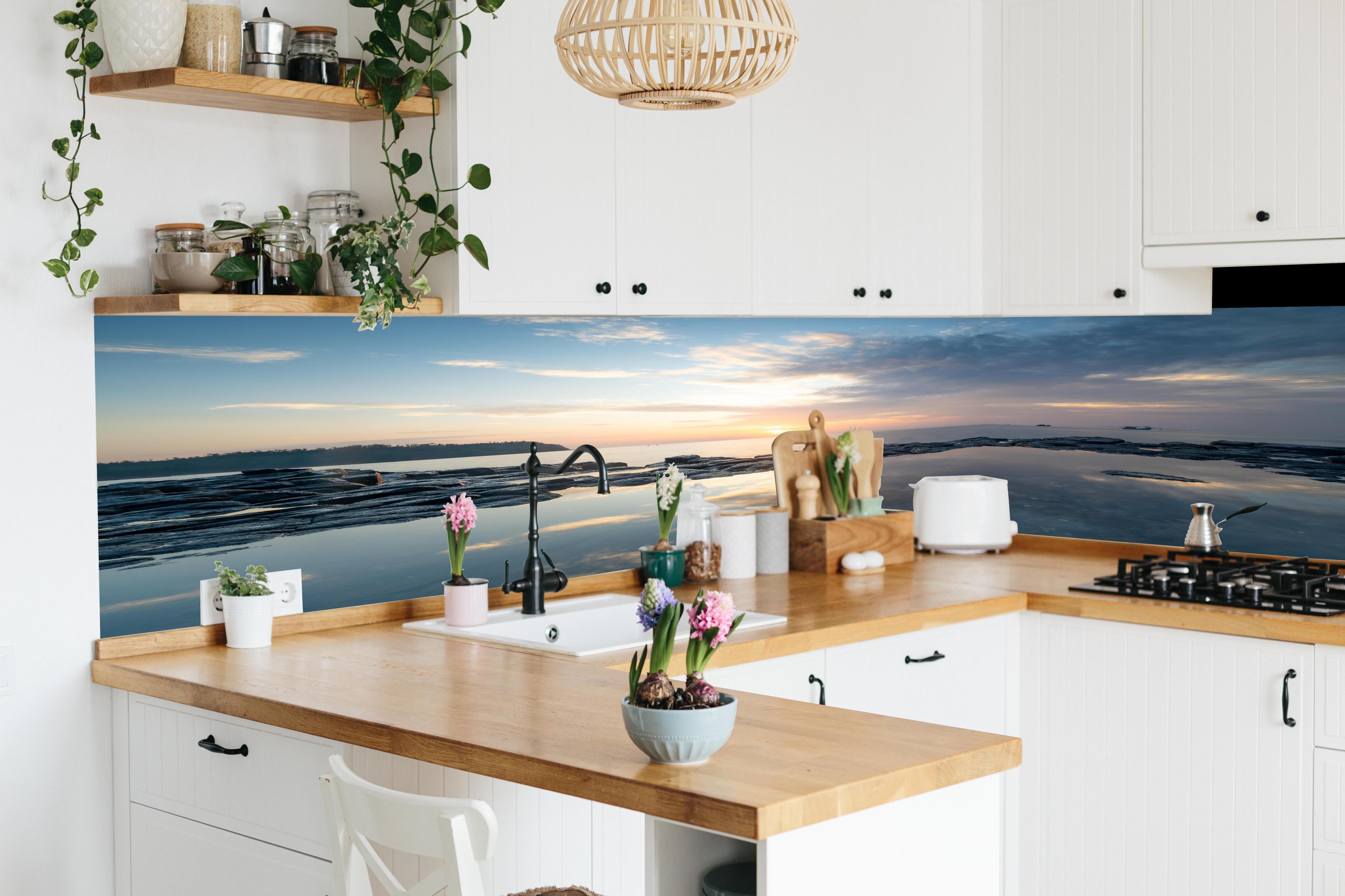 Küche - Pittoresker Sonnenuntergang über dem ruhigen Meer mit reflektierendem Wasser hinter weißen Hochglanz-Küchenregalen und schwarzem Wasserhahn