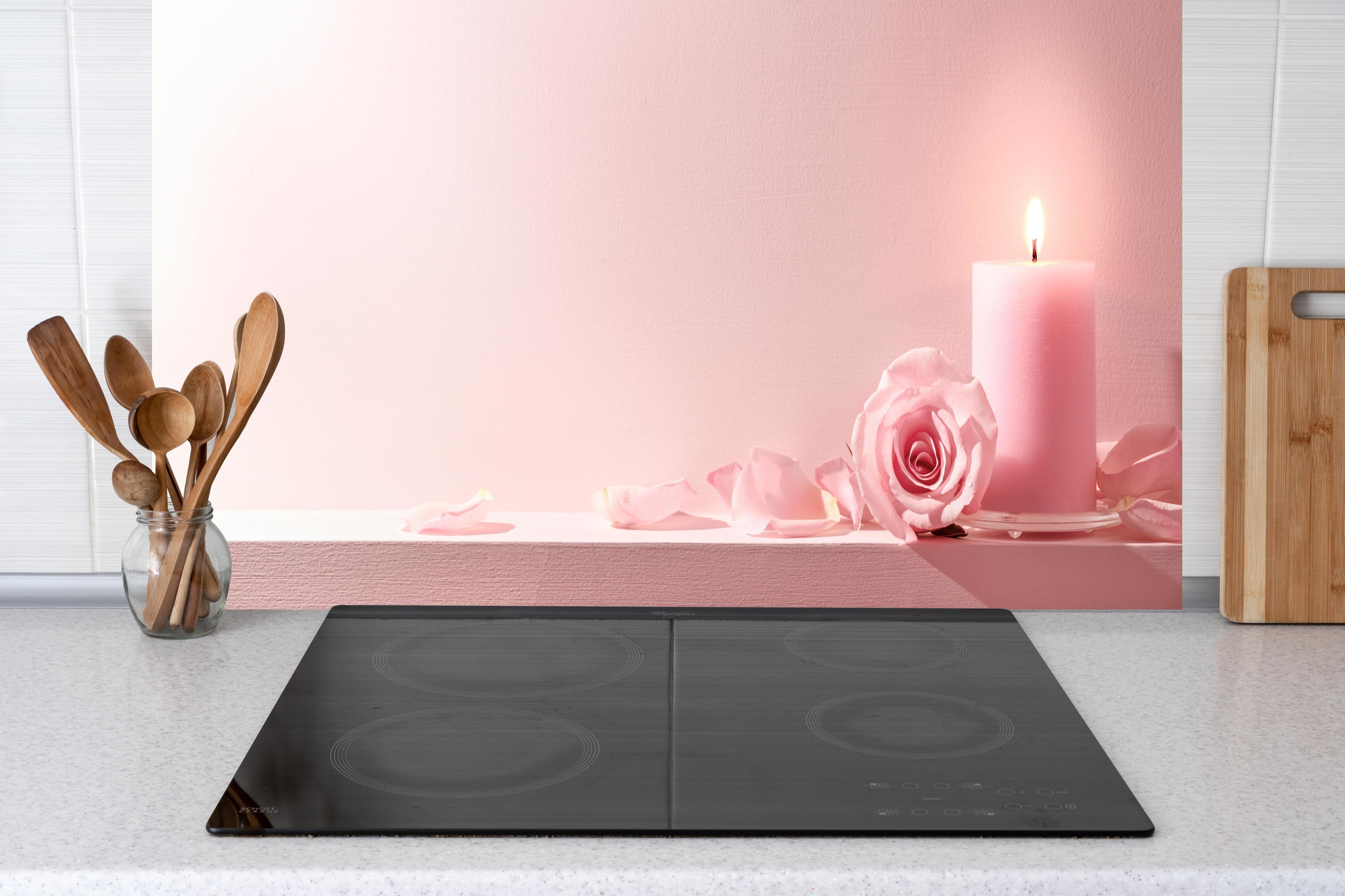 Küche - Rosa Rosen und Kerze auf einem rosa Hintergrund hinter weißen Hochglanz-Küchenregalen und schwarzem Wasserhahn
