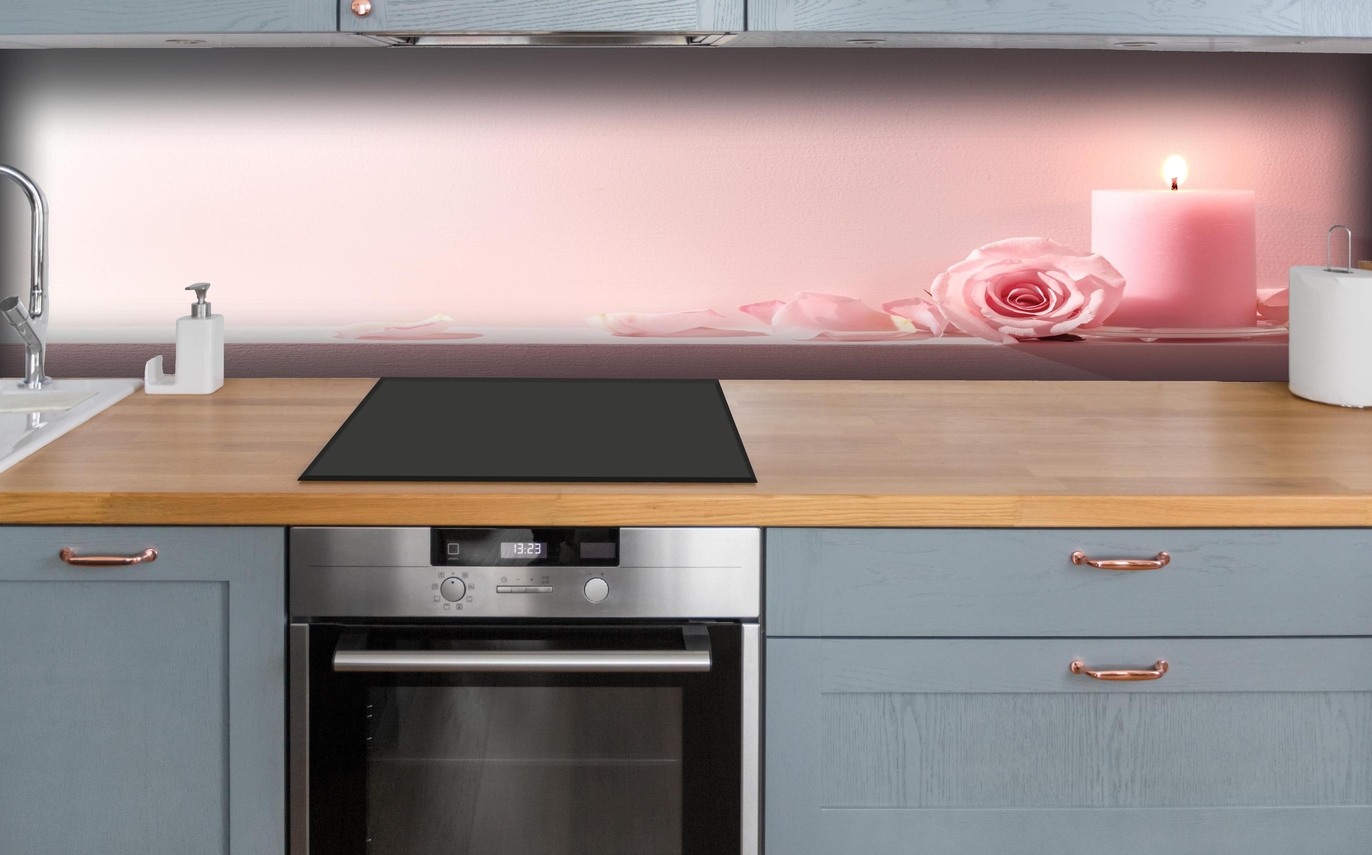 Küche - Rosa Rosen und Kerze auf einem rosa Hintergrund hinter weißen Hochglanz-Küchenregalen und schwarzem Wasserhahn