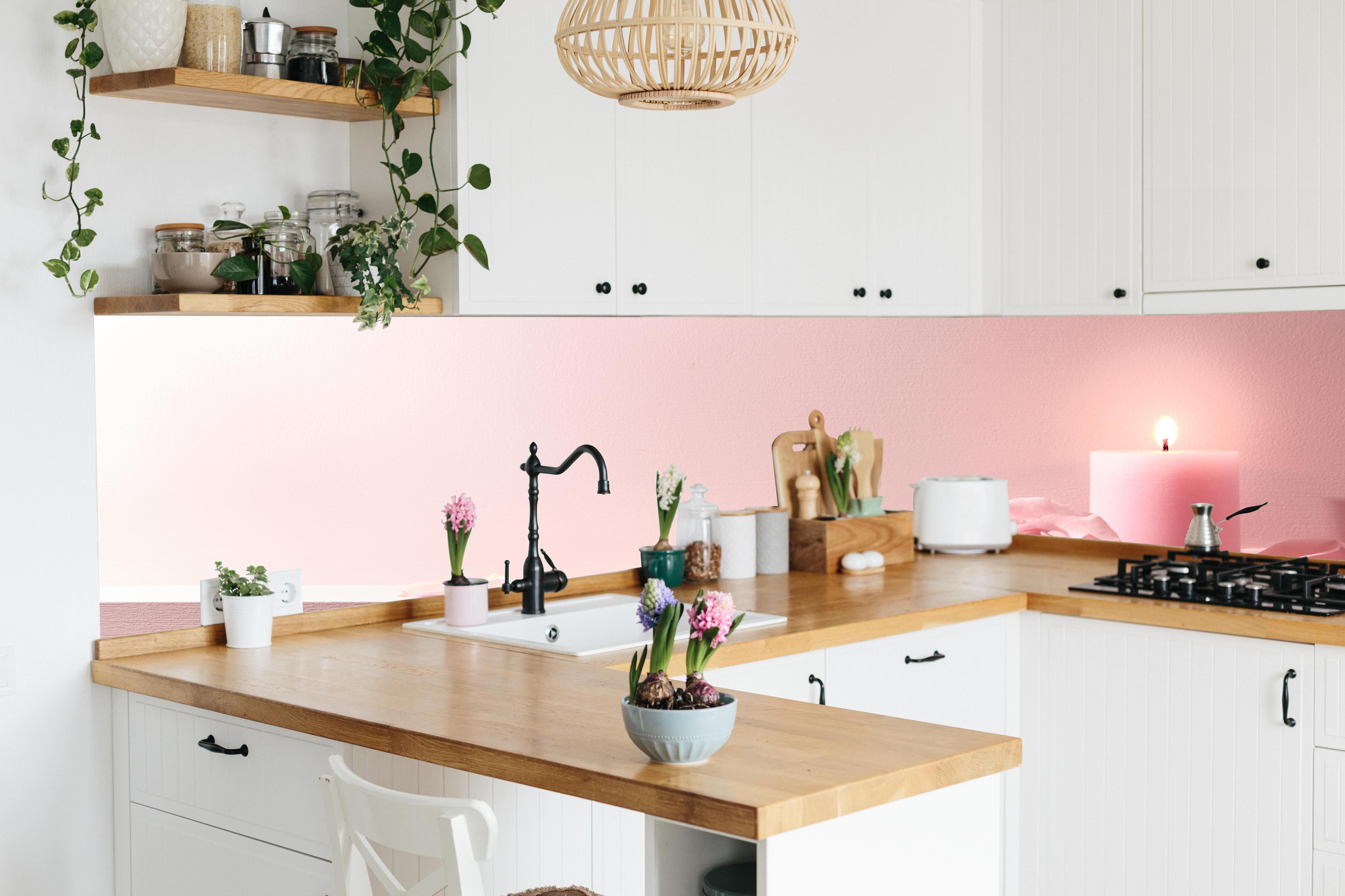 Küche - Rosa Rosen und Kerze auf einem rosa Hintergrund hinter weißen Hochglanz-Küchenregalen und schwarzem Wasserhahn
