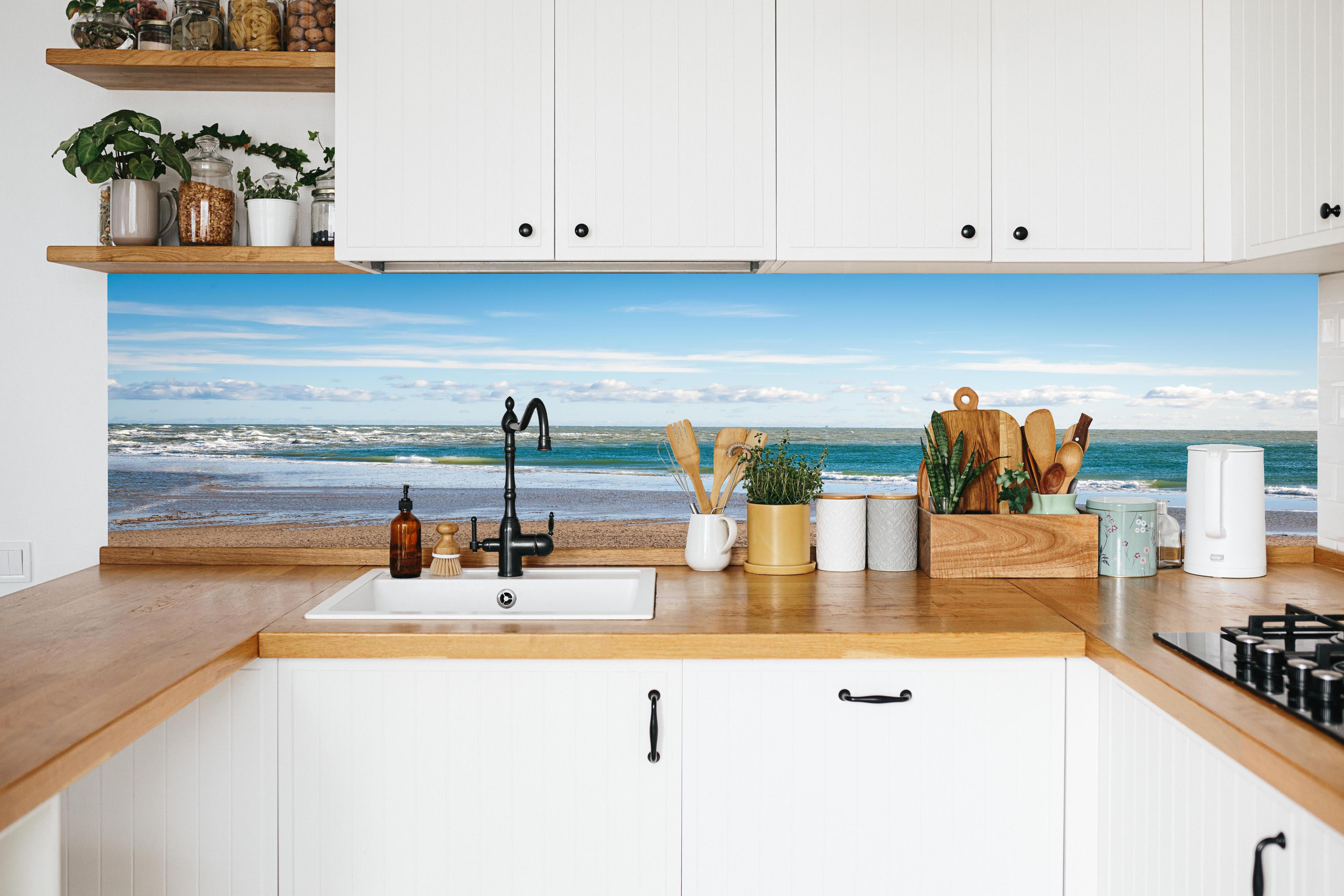 Küche - Ruhige Küstenlandschaft unter blauem Himmel mit sanften Wellen und feinem Sand hinter weißen Hochglanz-Küchenregalen und schwarzem Wasserhahn