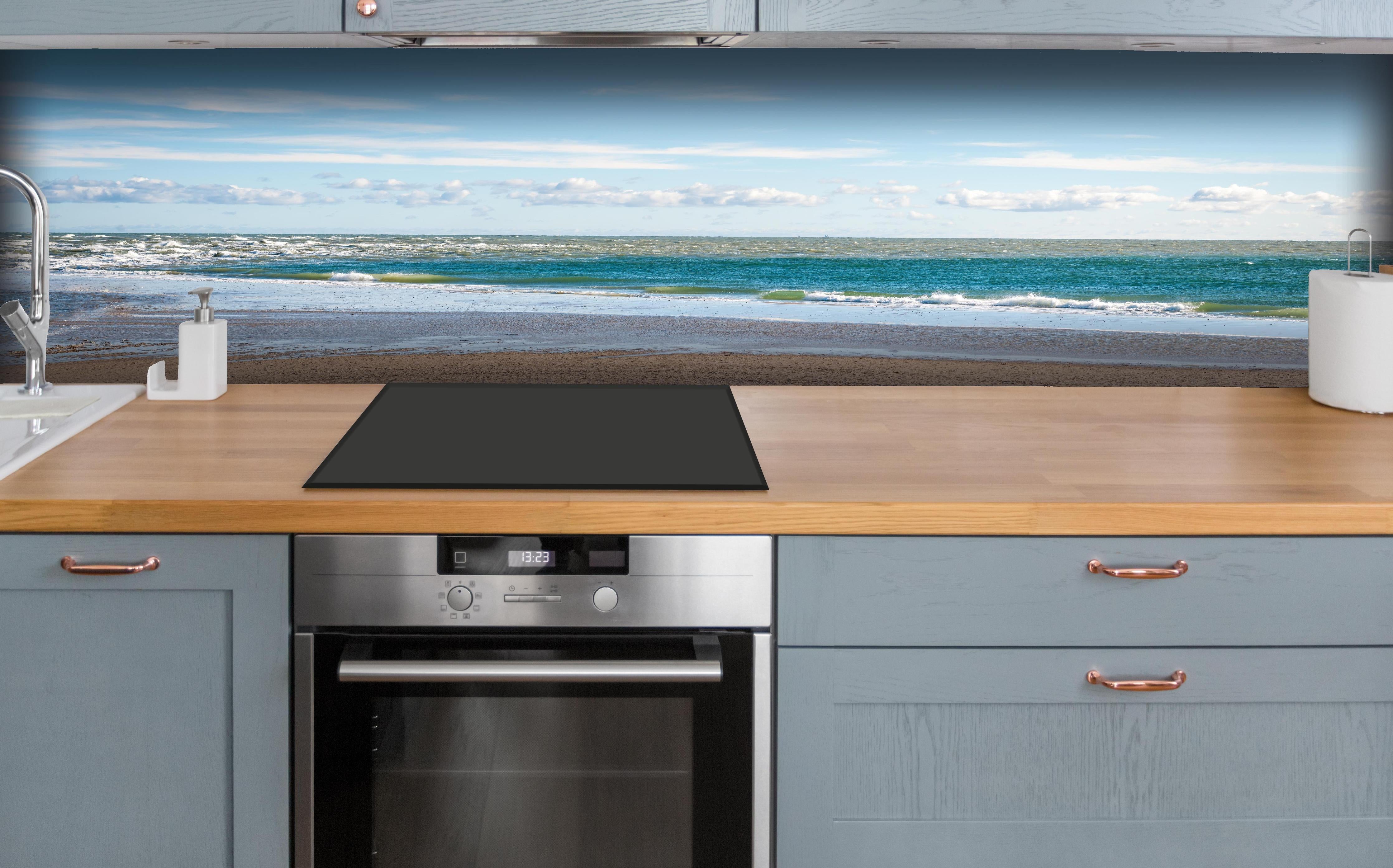 Küche - Ruhige Küstenlandschaft unter blauem Himmel mit sanften Wellen und feinem Sand hinter weißen Hochglanz-Küchenregalen und schwarzem Wasserhahn