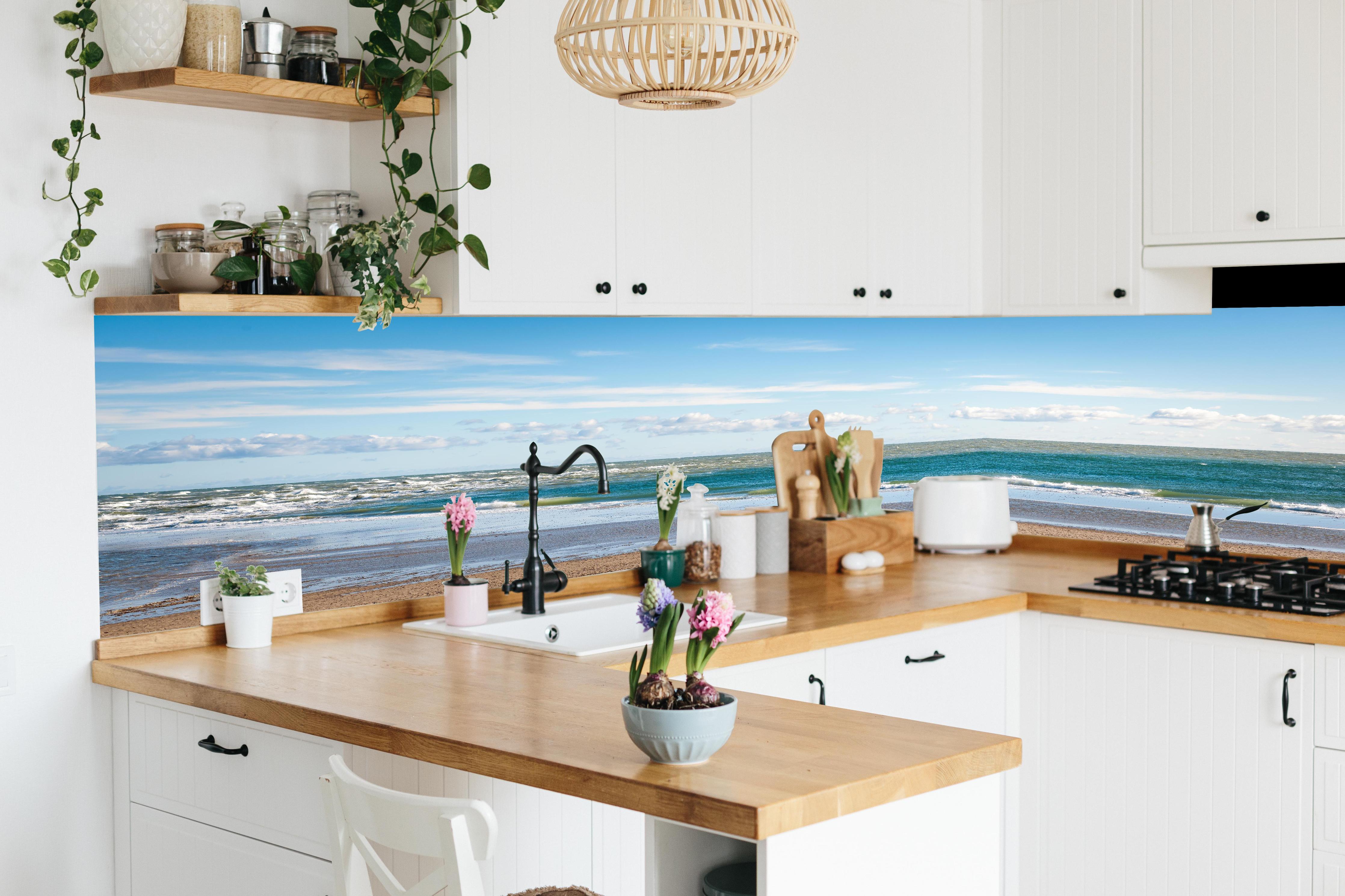 Küche - Ruhige Küstenlandschaft unter blauem Himmel mit sanften Wellen und feinem Sand hinter weißen Hochglanz-Küchenregalen und schwarzem Wasserhahn