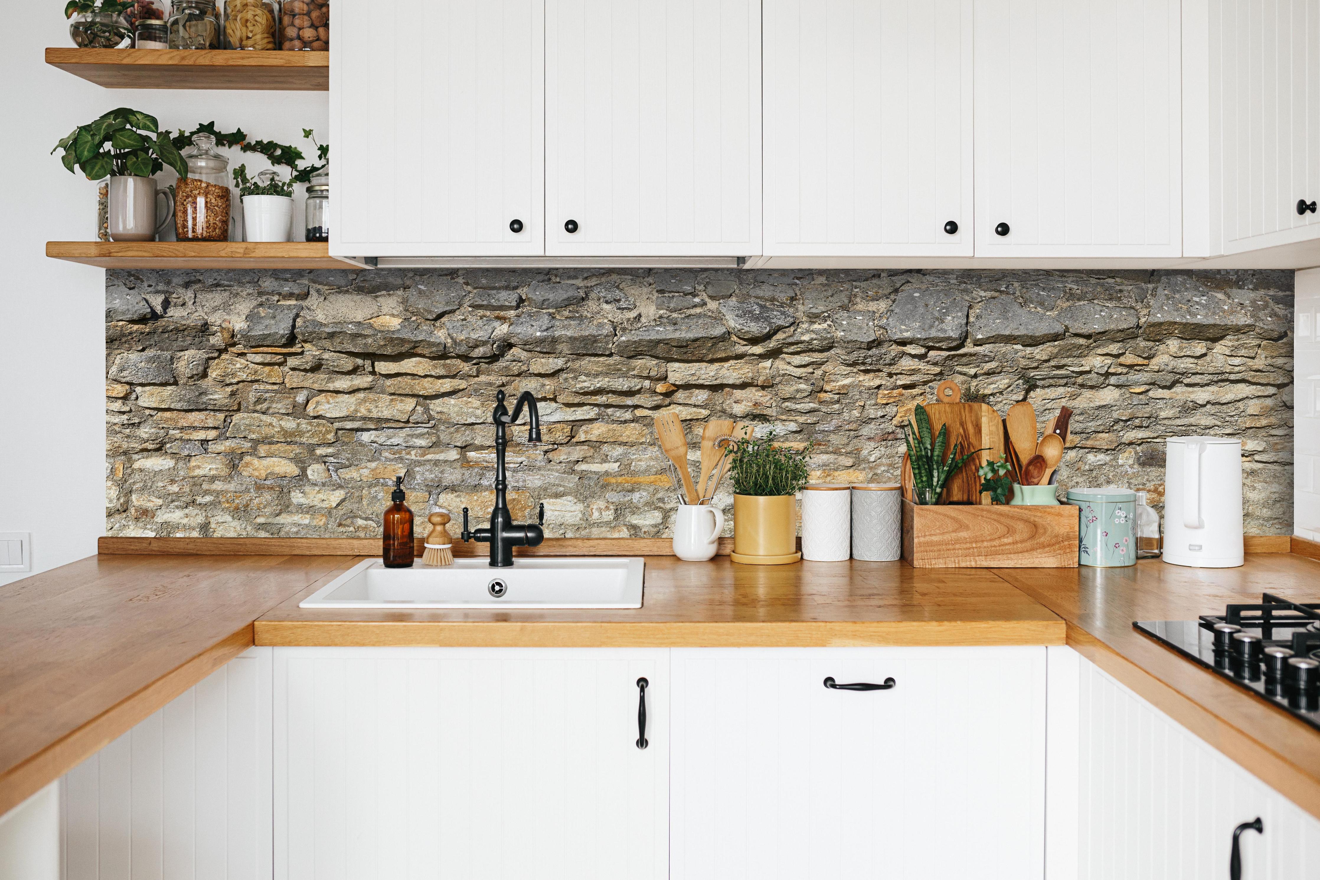 Küche - Rustikale Burgmauer hinter weißen Hochglanz-Küchenregalen und schwarzem Wasserhahn