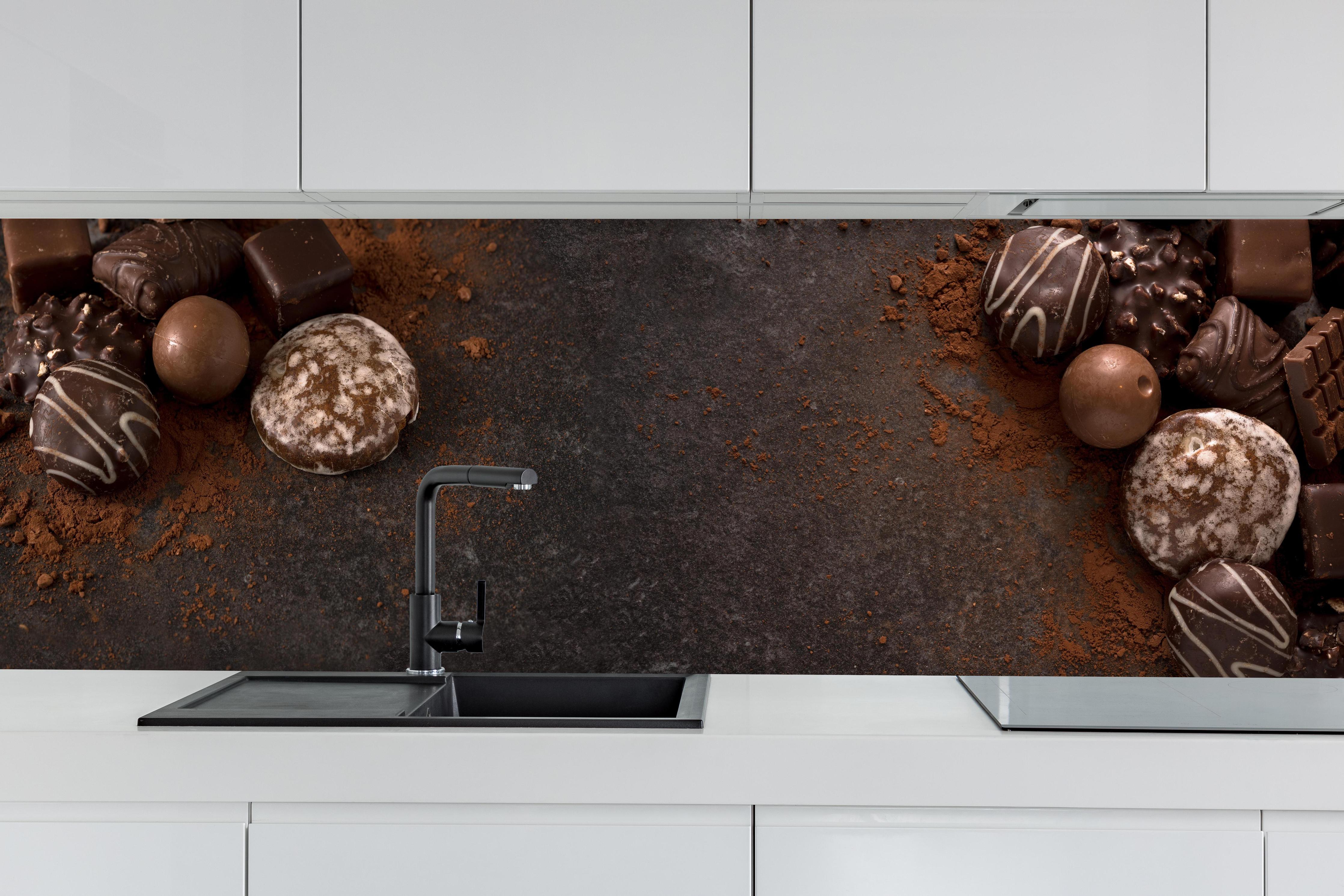 Küche - Schokoladenpralinen auf Schieferuntergrund hinter weißen Hochglanz-Küchenregalen und schwarzem Wasserhahn