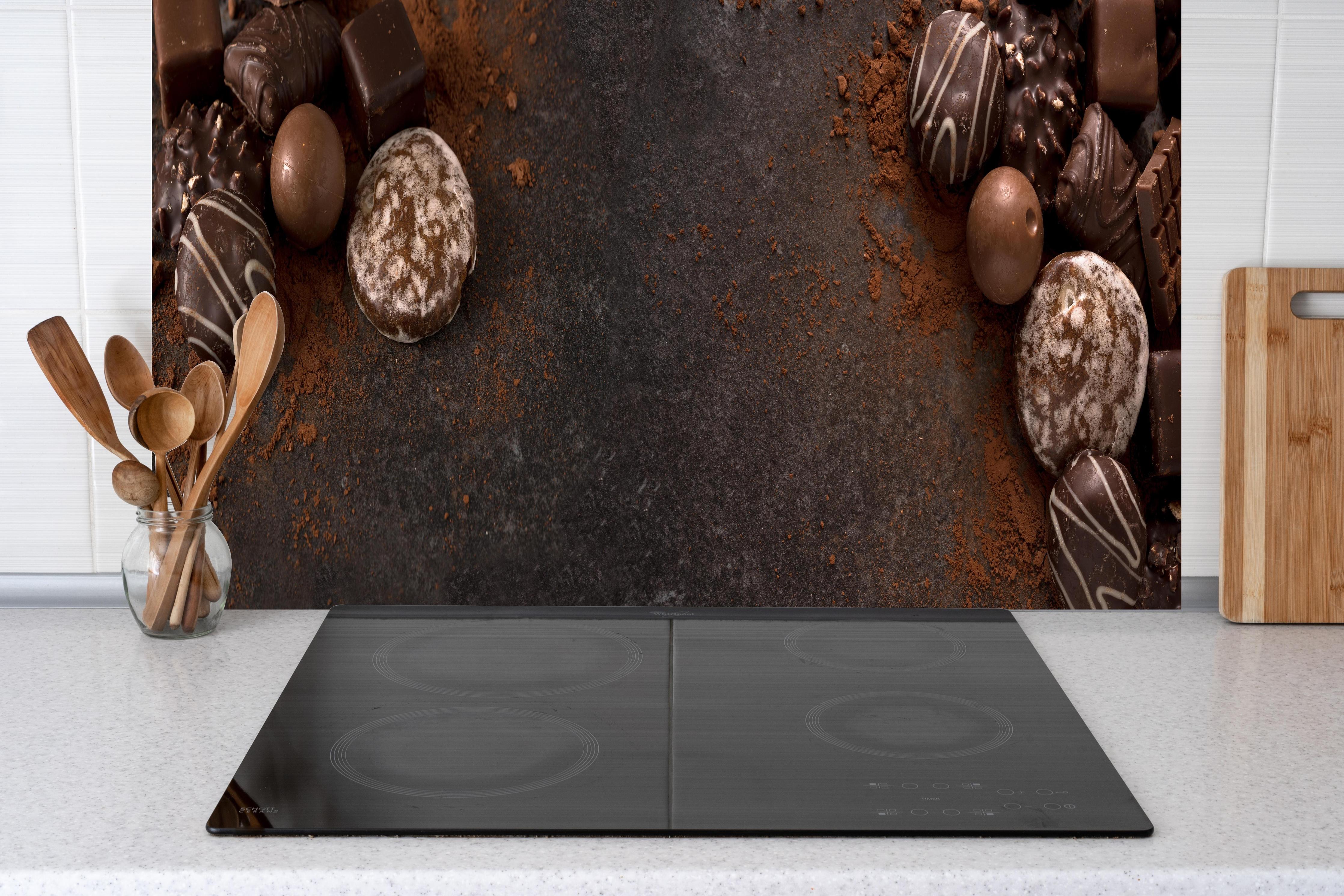 Küche - Schokoladenpralinen auf Schieferuntergrund hinter weißen Hochglanz-Küchenregalen und schwarzem Wasserhahn