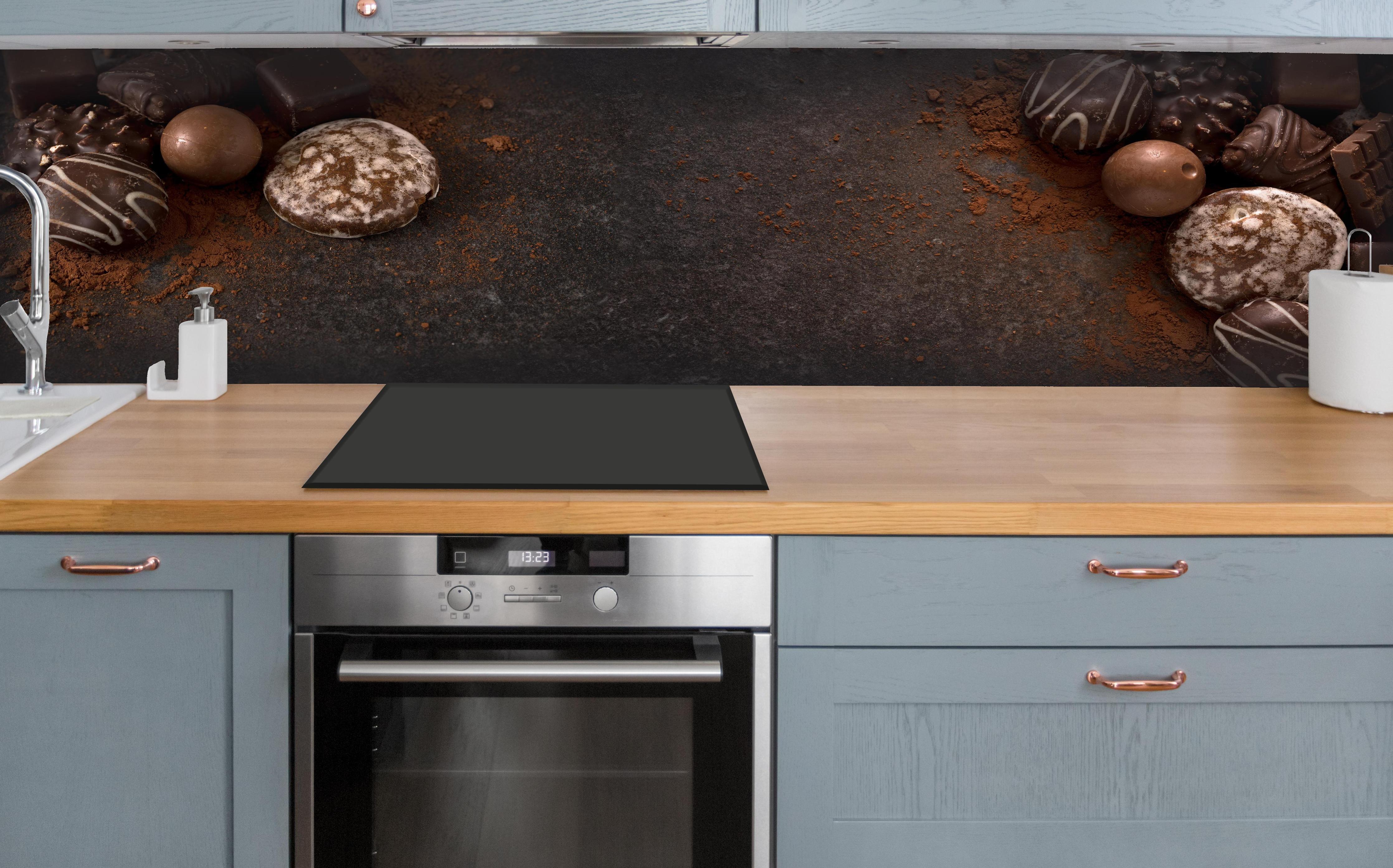 Küche - Schokoladenpralinen auf Schieferuntergrund hinter weißen Hochglanz-Küchenregalen und schwarzem Wasserhahn