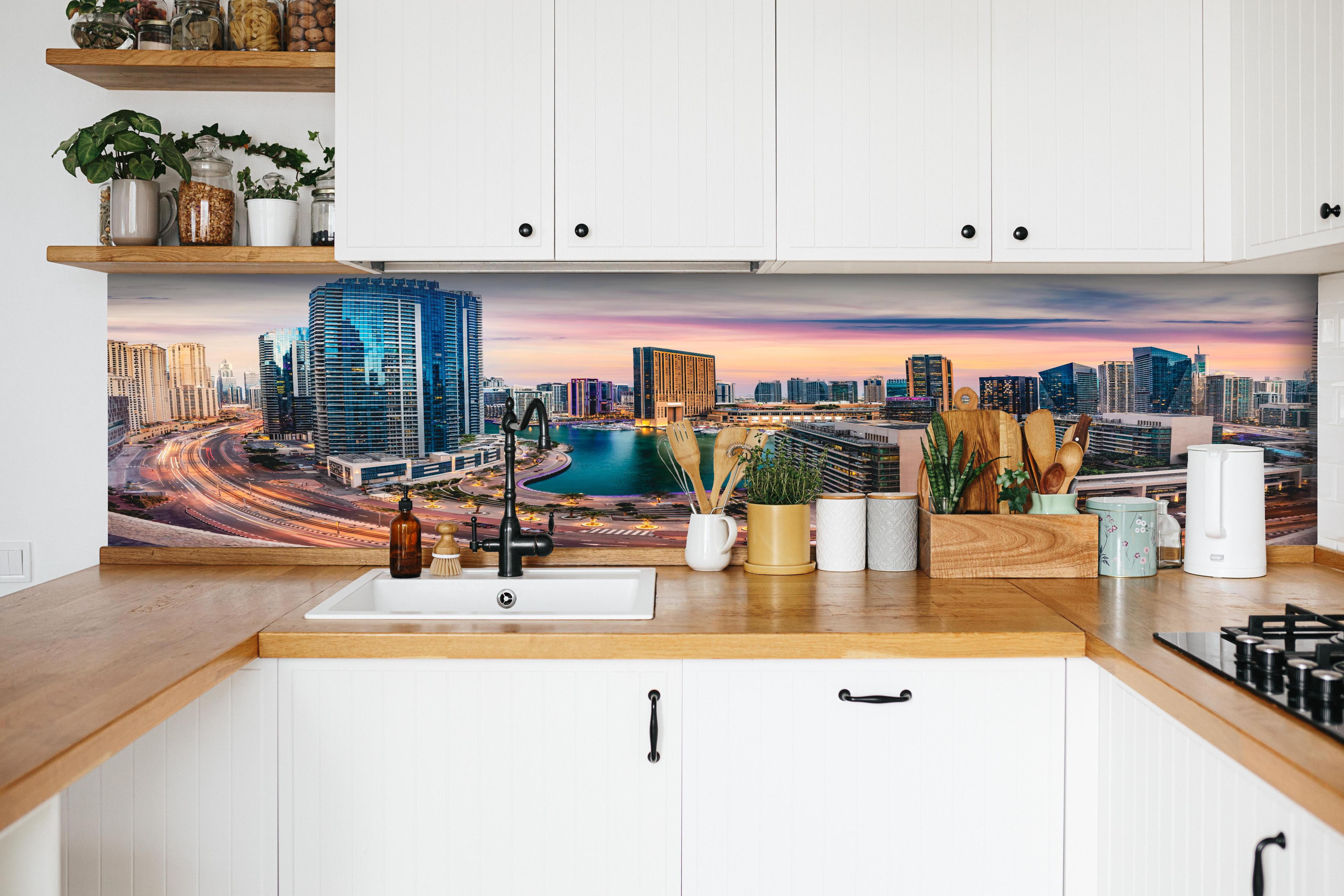 Küche - Skyline des Jachthafens von Dubai bei Sonnenuntergang hinter weißen Hochglanz-Küchenregalen und schwarzem Wasserhahn