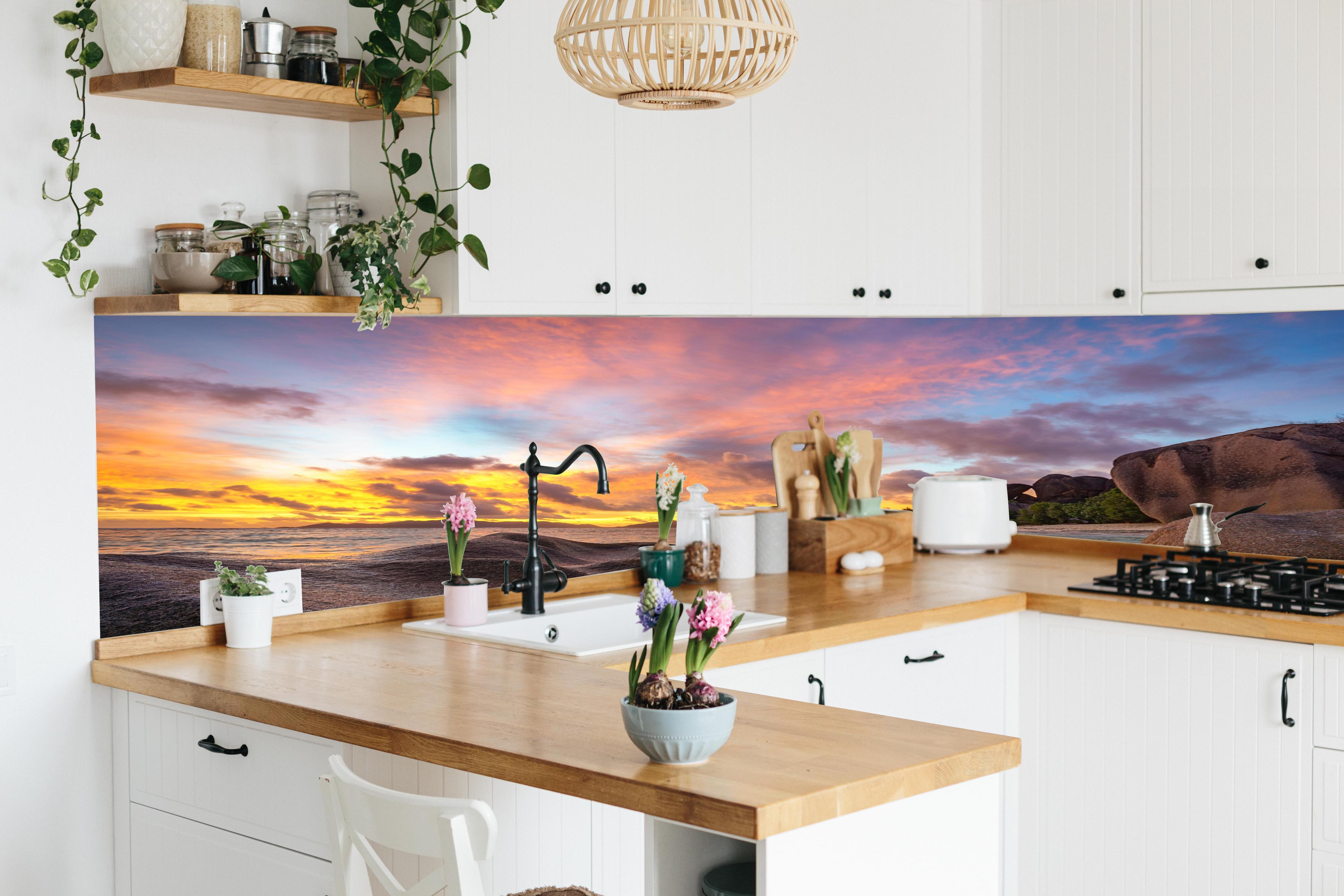Küche - Sonnenuntergang am tropischen Strand hinter weißen Hochglanz-Küchenregalen und schwarzem Wasserhahn
