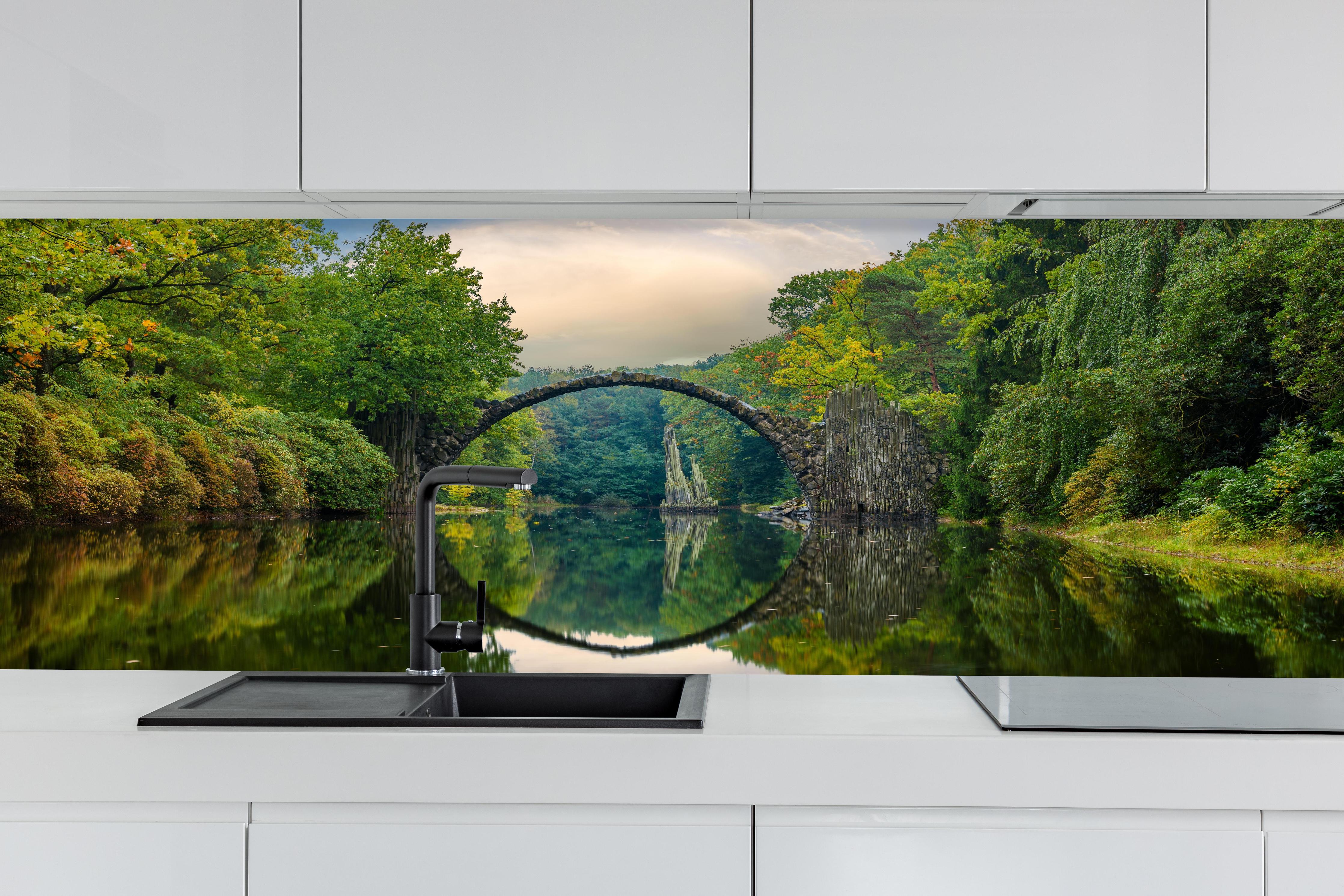 Küche - Steinbrücke über Fluss im Wald hinter weißen Hochglanz-Küchenregalen und schwarzem Wasserhahn