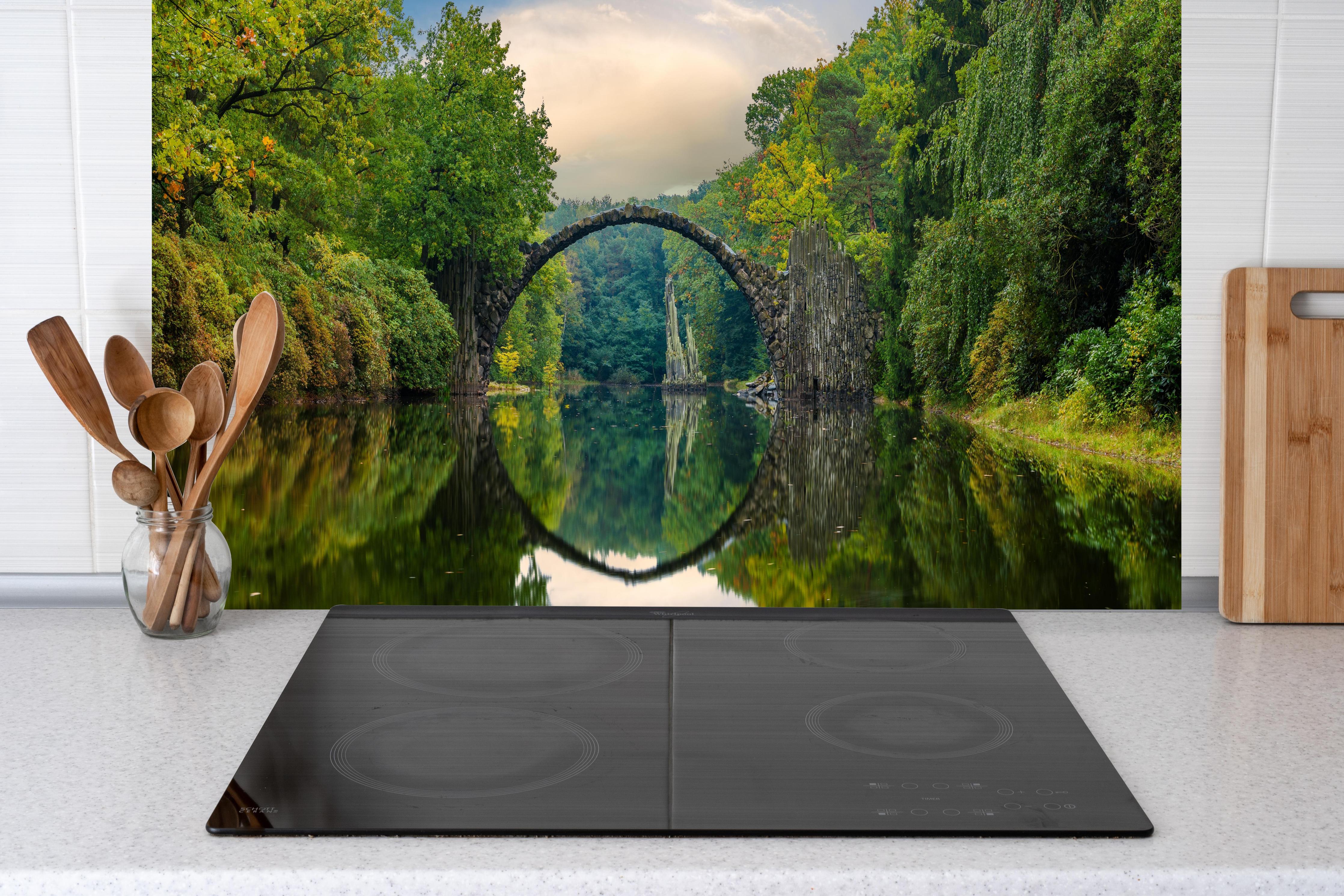 Küche - Steinbrücke über Fluss im Wald hinter weißen Hochglanz-Küchenregalen und schwarzem Wasserhahn