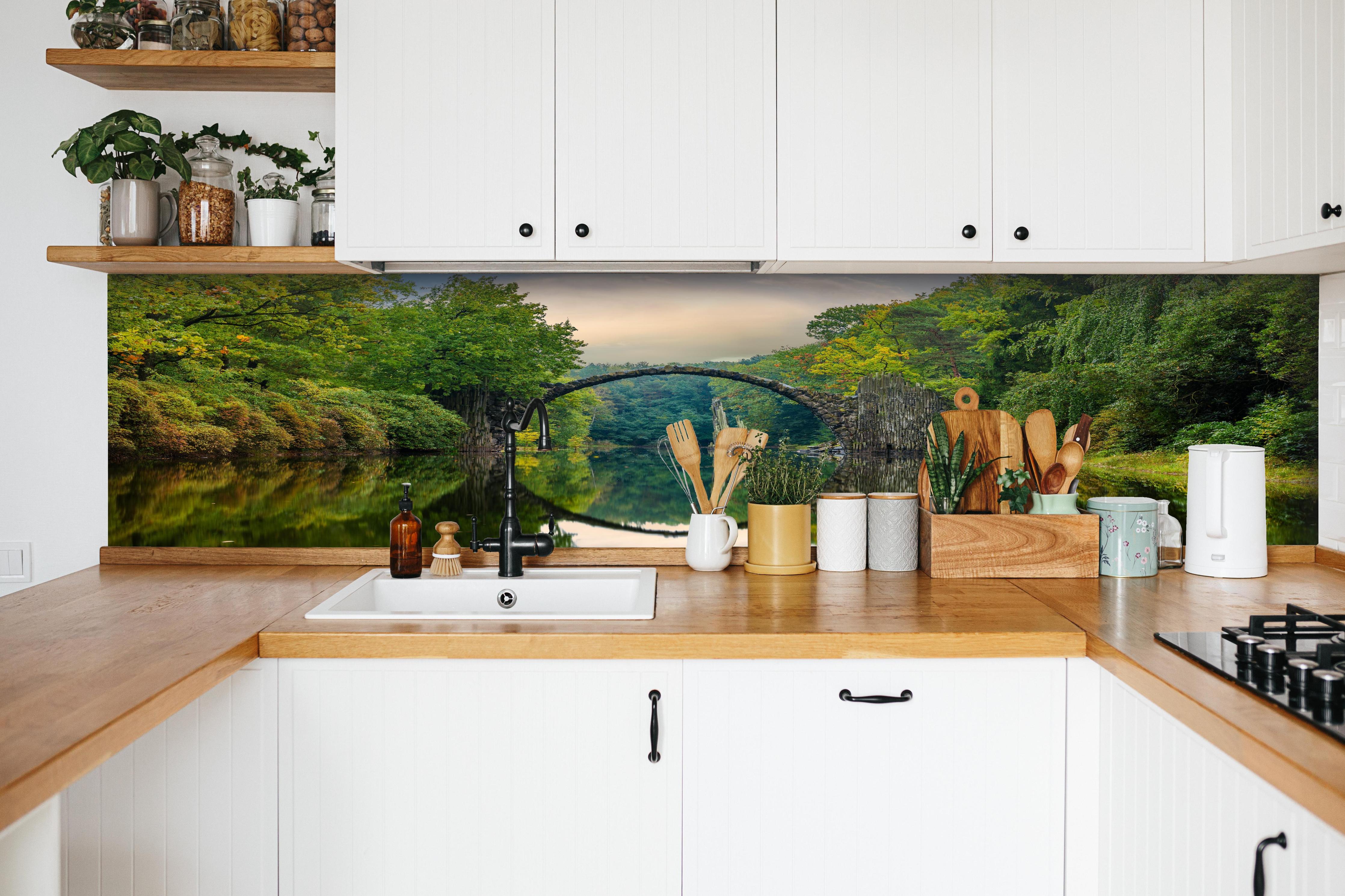 Küche - Steinbrücke über Fluss im Wald hinter weißen Hochglanz-Küchenregalen und schwarzem Wasserhahn