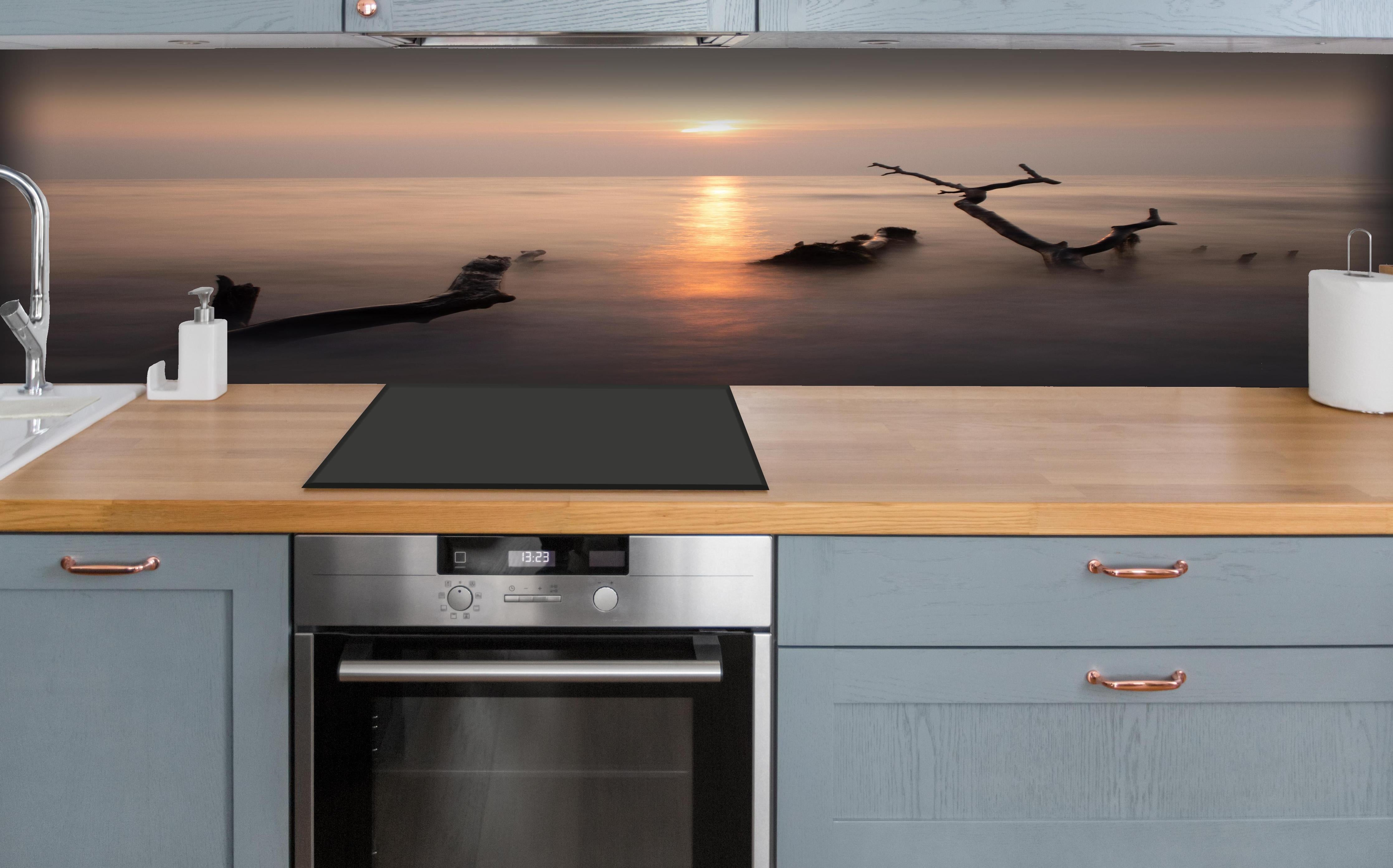 Küche - Stimmungsvoller Sonnenuntergangs-Strand hinter weißen Hochglanz-Küchenregalen und schwarzem Wasserhahn